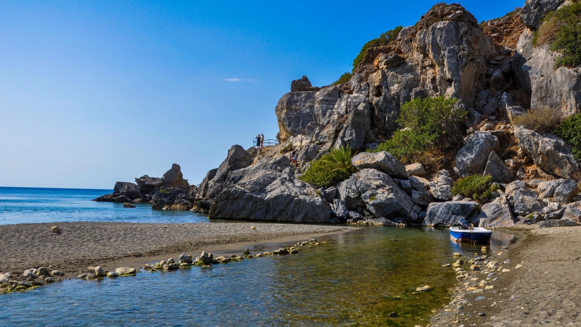 Scenic view of Preveli Beach with its palm forest, rock formations, and the turquoise waters of the Mediterranean Sea.