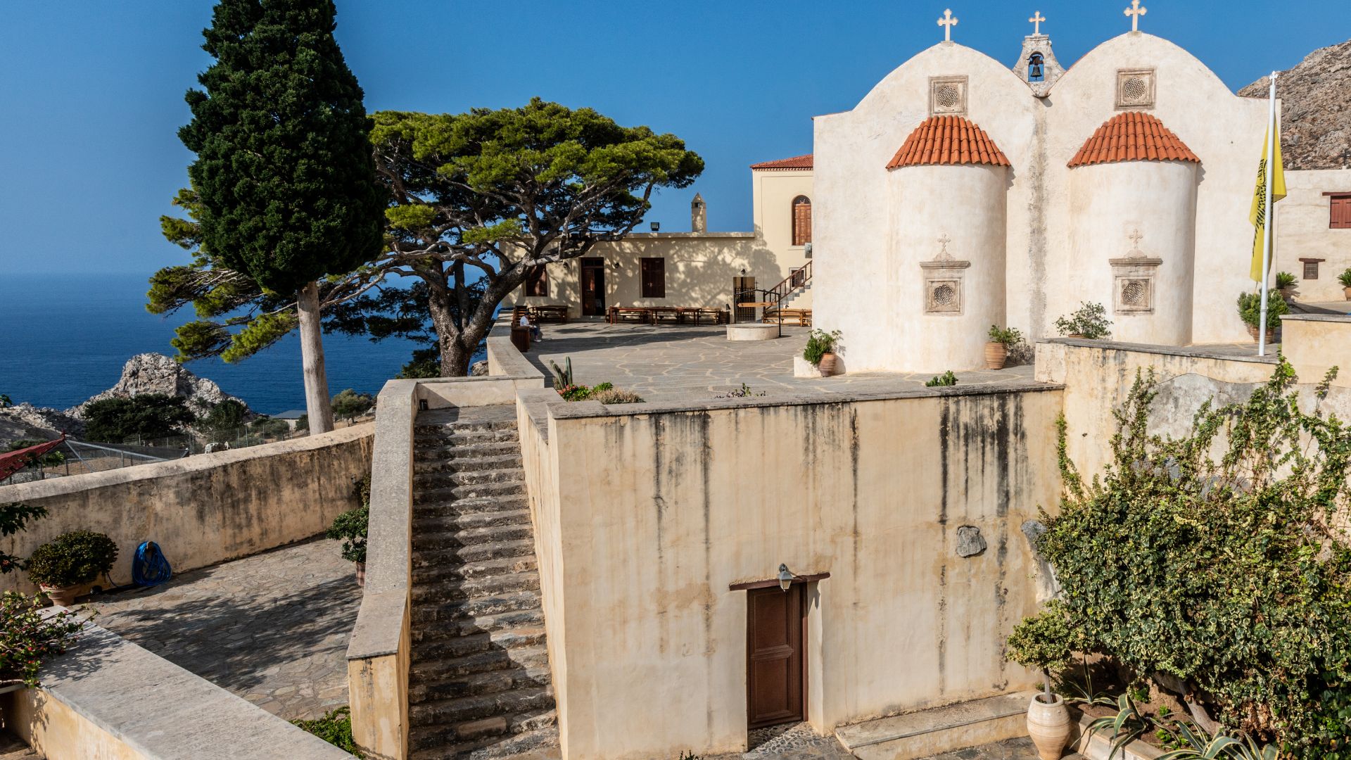 Exterior view of Preveli Monastery with white buildings and a stone courtyard.