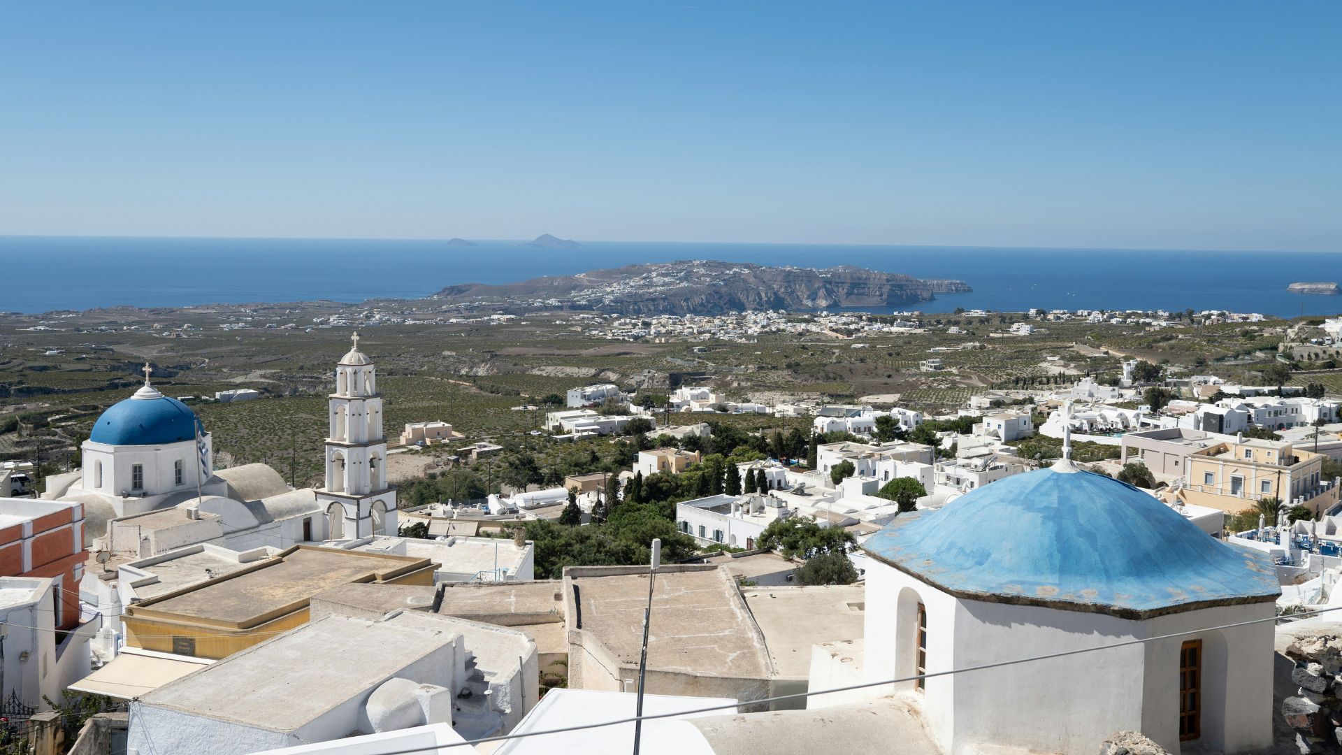Panoramic view of Pyrgos village in Santorini, Greece with blue domes and whitewashed buildings.