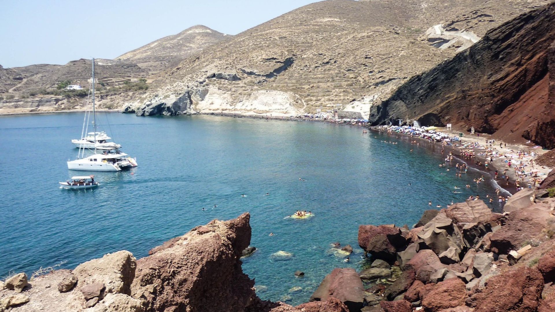 Scenic view or rocky cliffs, blue sea, and some boats at Red beach, Santorini, Greece.