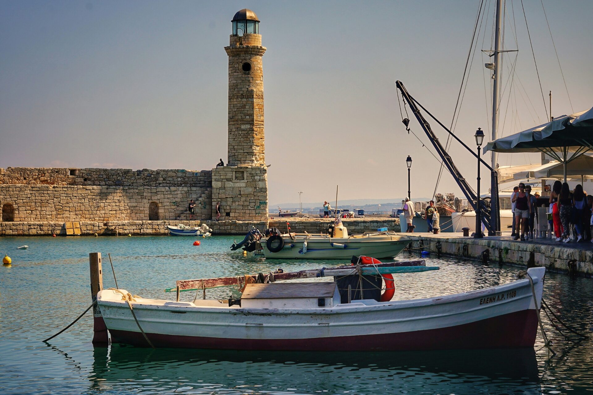 Rethymno’s coastal harbor with boats moored along the waterfront and the historic Venetian lighthouse standing at the edge of the pier