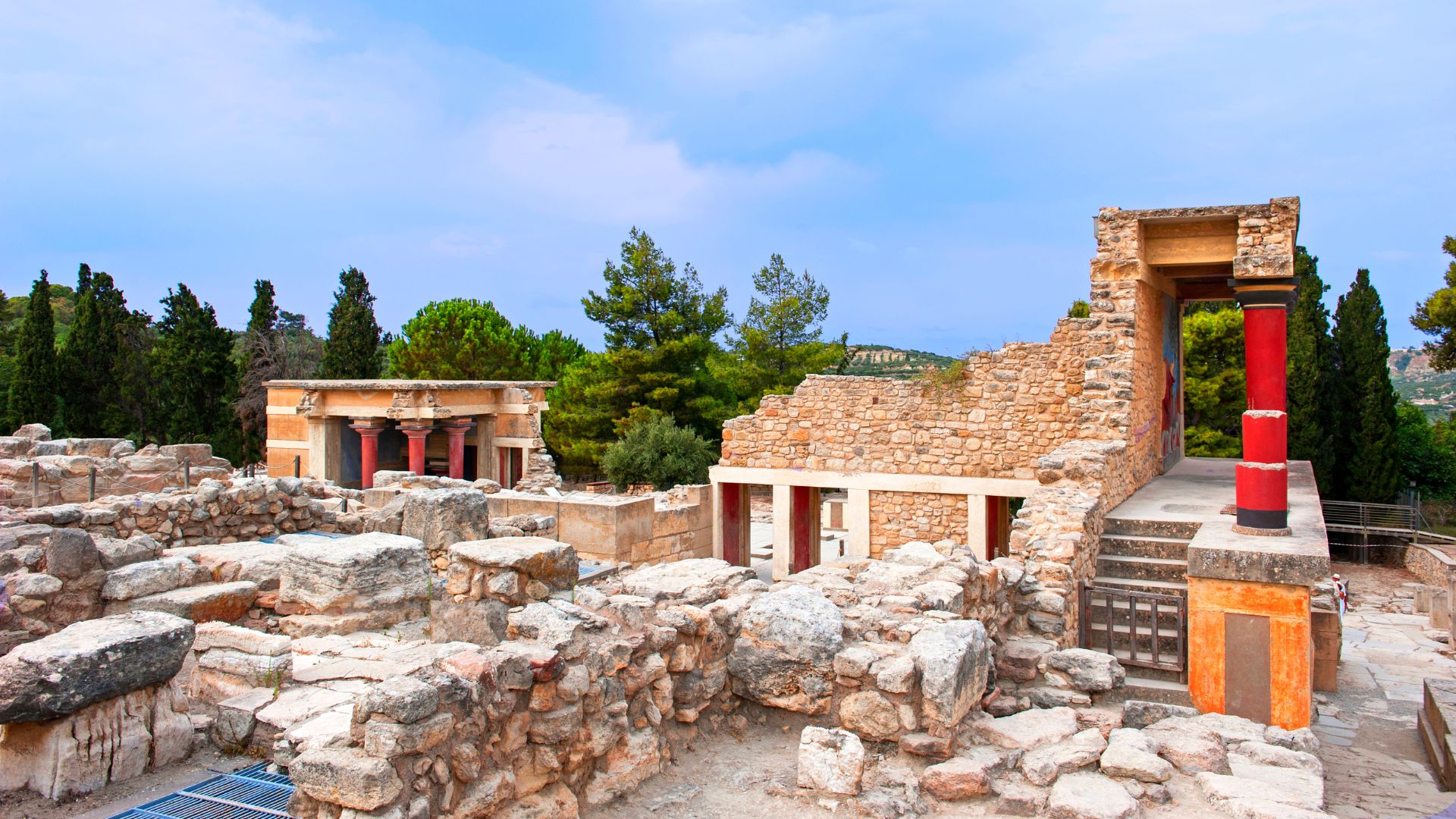 Ruins of the ancient Minoan palace of Knossos in Crete, featuring stone structures and columns under a blue sky.