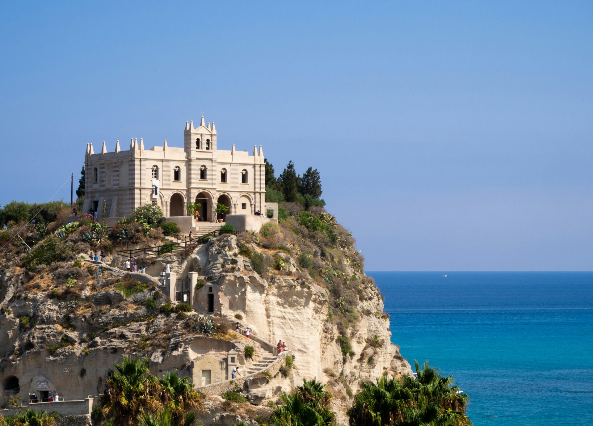 Santa Maria dell’Isola monastery perched atop a rocky promontory in Tropea, Italy, surrounded by lush gardens and overlooking the turquoise waters of the Tyrrhenian Sea.