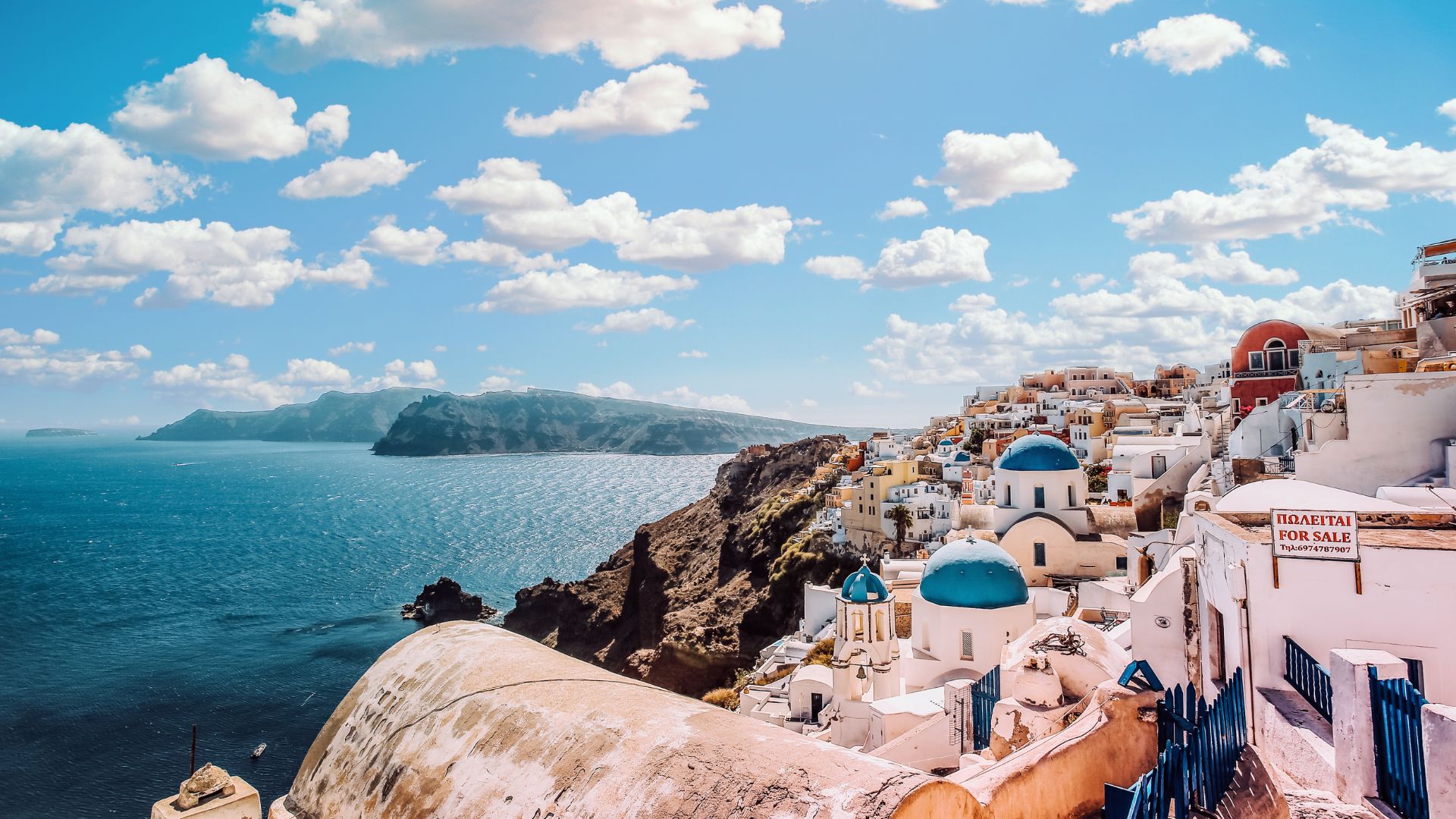 A scenic view of Santorini with its iconic white buildings and blue domes overlooking the Aegean Sea.