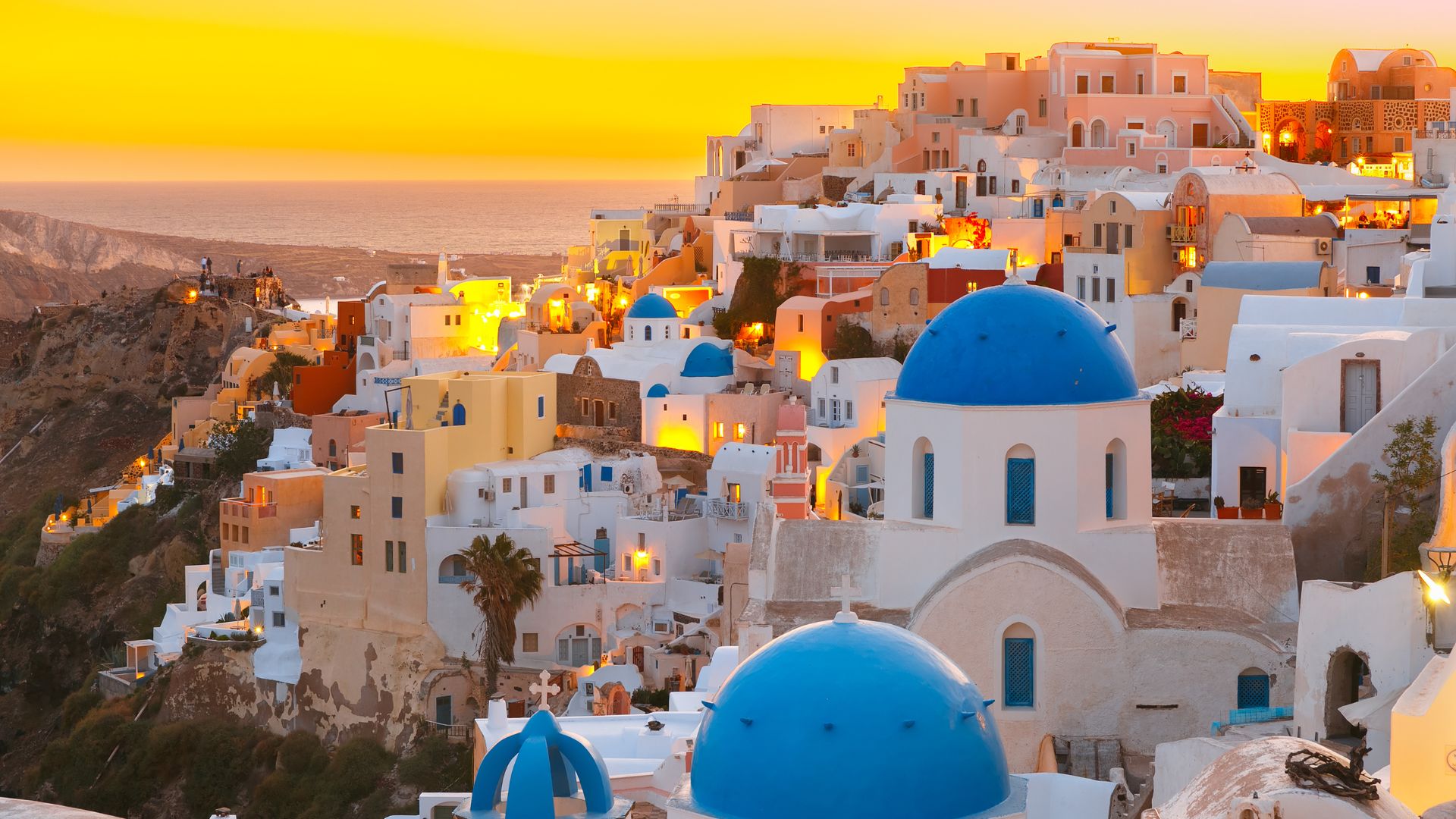 A picturesque view of Oia village in Santorini, Greece, with its iconic white buildings and blue domes, set against a vibrant sunset sky.