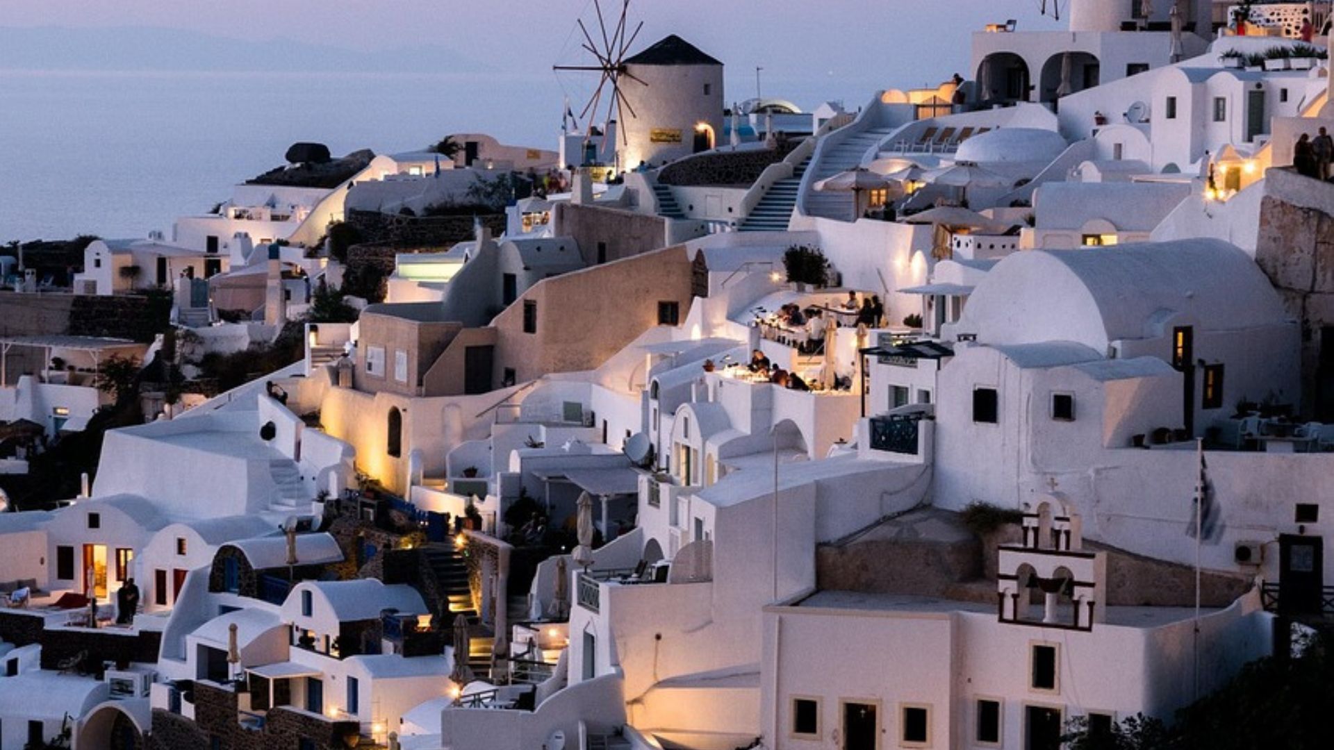 A picturesque view of Santorini at dusk, with its iconic white buildings and windmills.