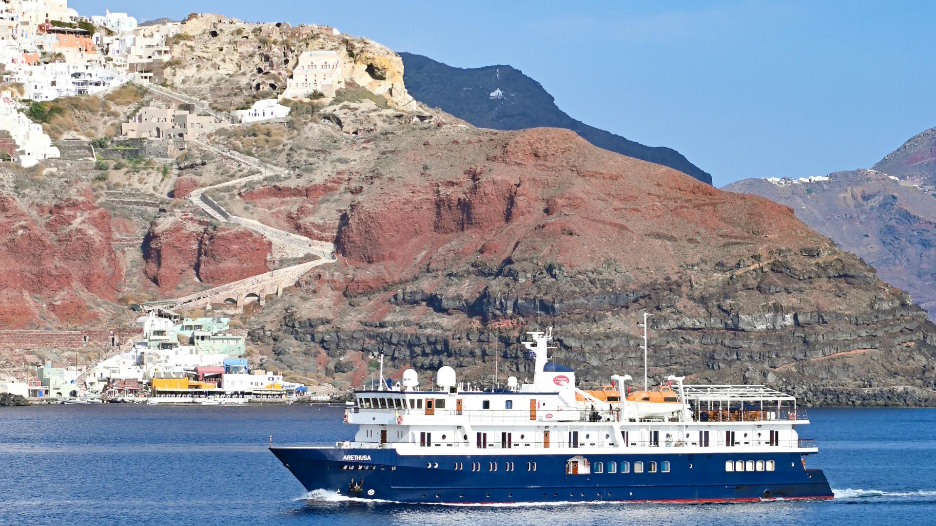 A cruise ship in the Aegean Sea, with the volcanic island of Santorini in the background.