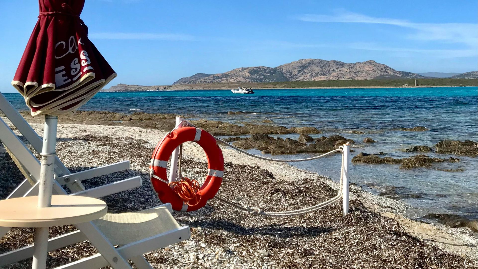A scenic view of La Pelosa Beach in Sardinia, featuring turquoise water, an umbrella and chair.