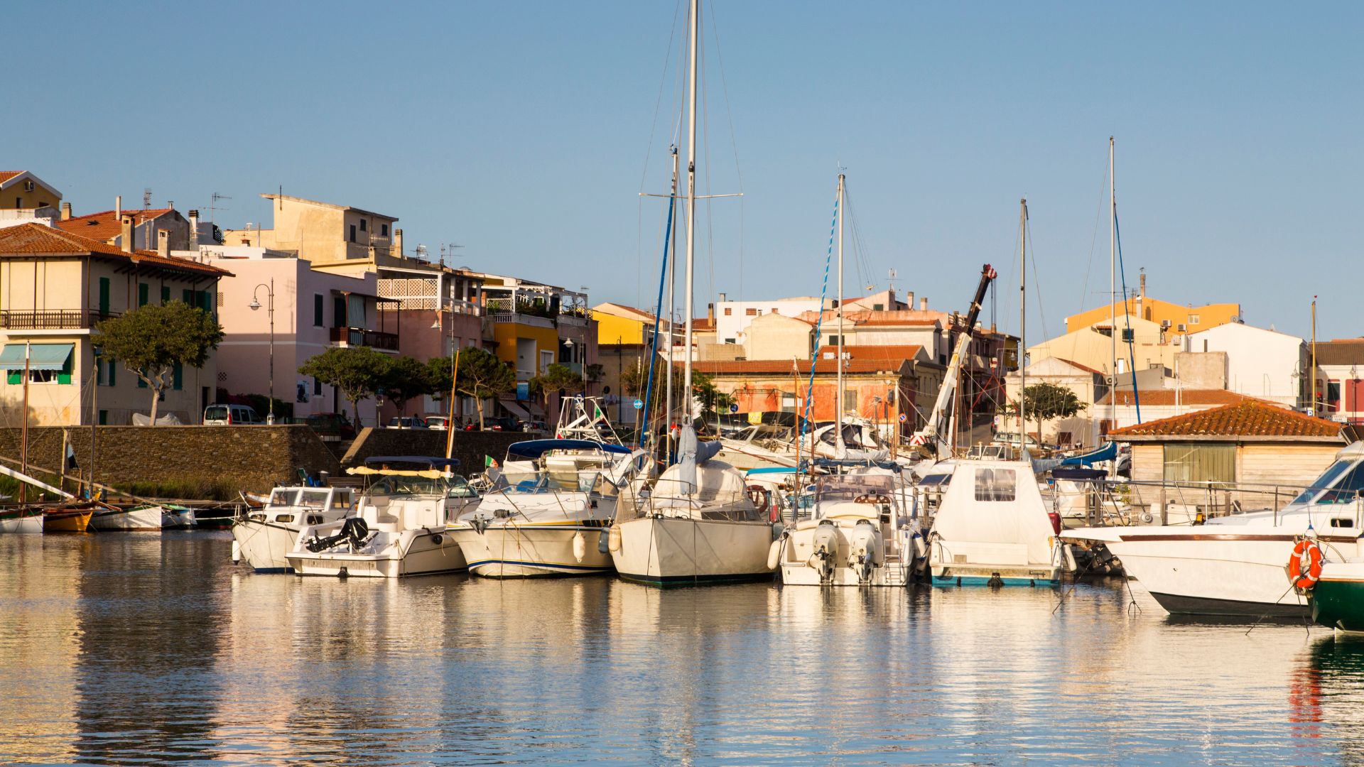 Boats docked in the harbor of Stintino, Sardinia, with colorful buildings in the background under a clear blue sky.