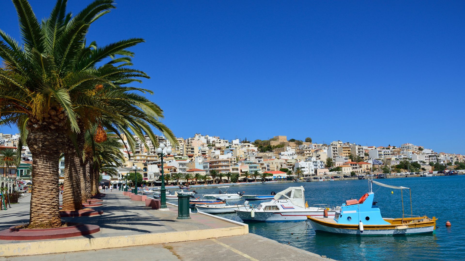 A scenic view of Sitia harbor with colorful boats and hillside town.