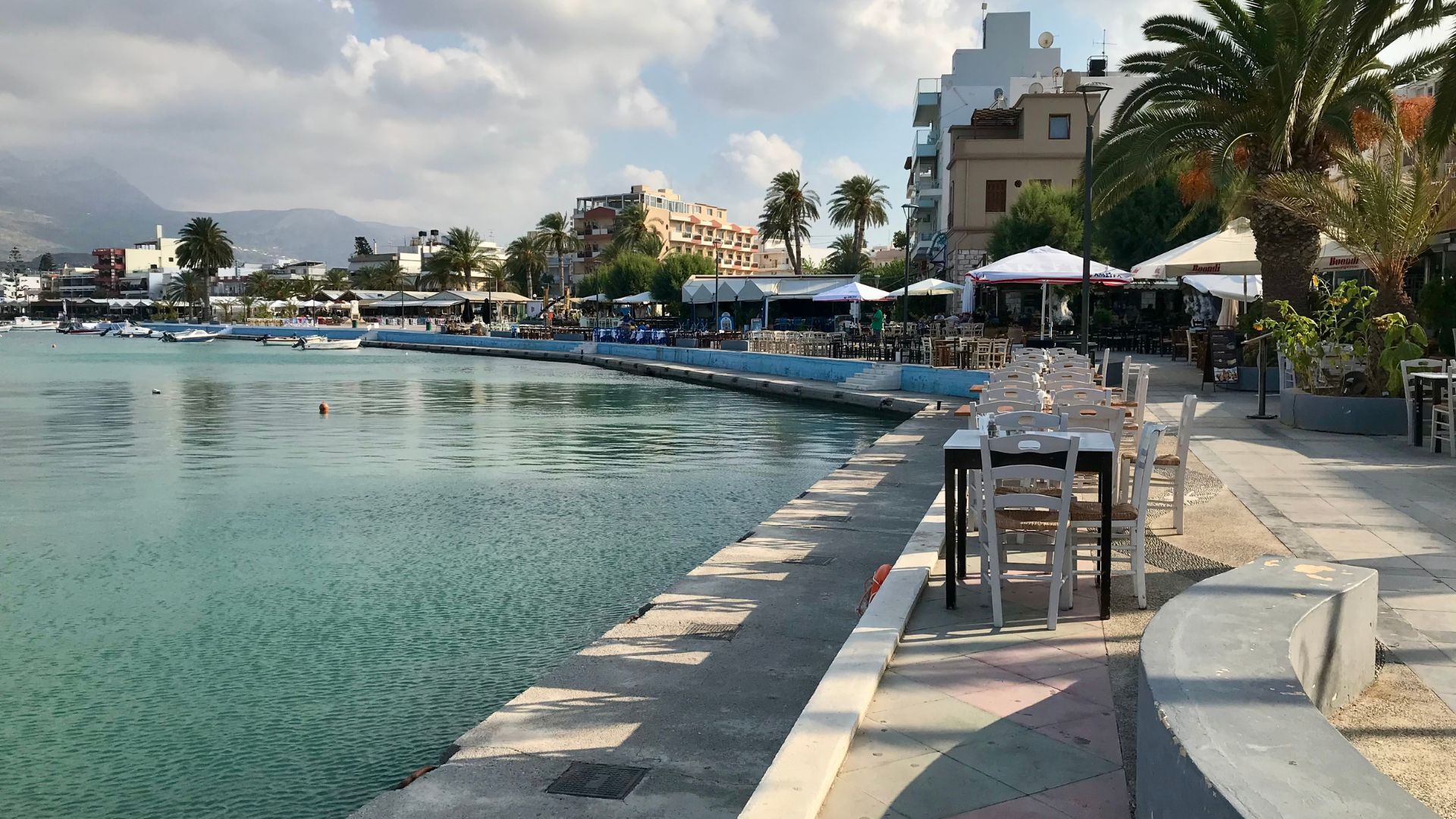 A scenic view of Sitia's harbor, with calm water, boats, and waterfront restaurants.