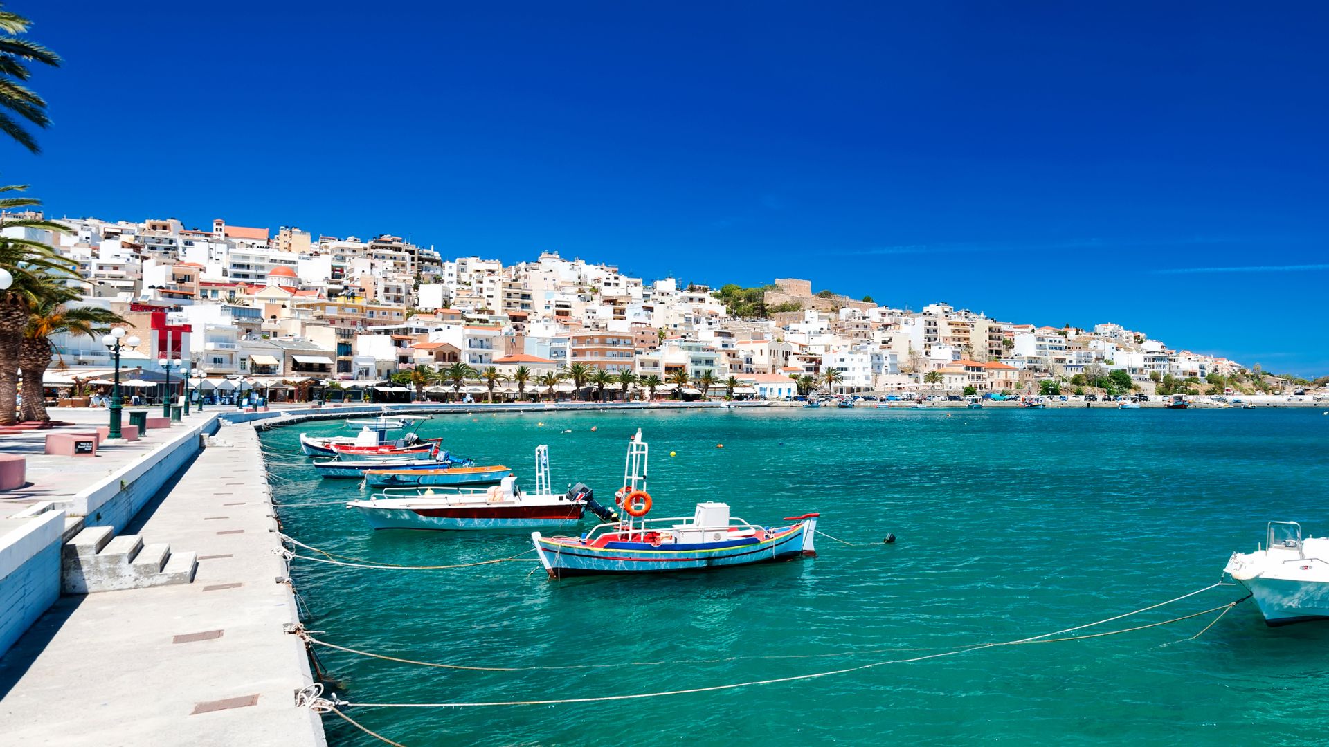 A scenic view of Sitia harbor with colorful boats and hillside town.