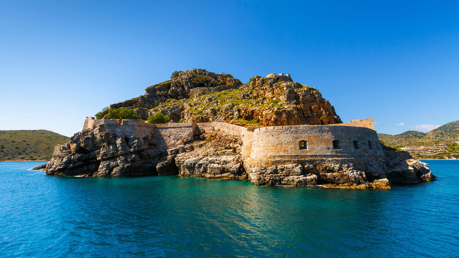 Closer look on Spinalonga Island, Crete, featuring the Venetian fortress ruins surrounded by turquoise waters.