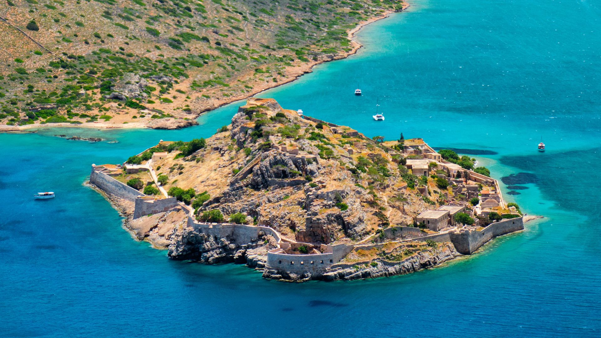 Aerial view of Spinalonga Island, Crete, featuring the Venetian fortress ruins surrounded by turquoise waters.