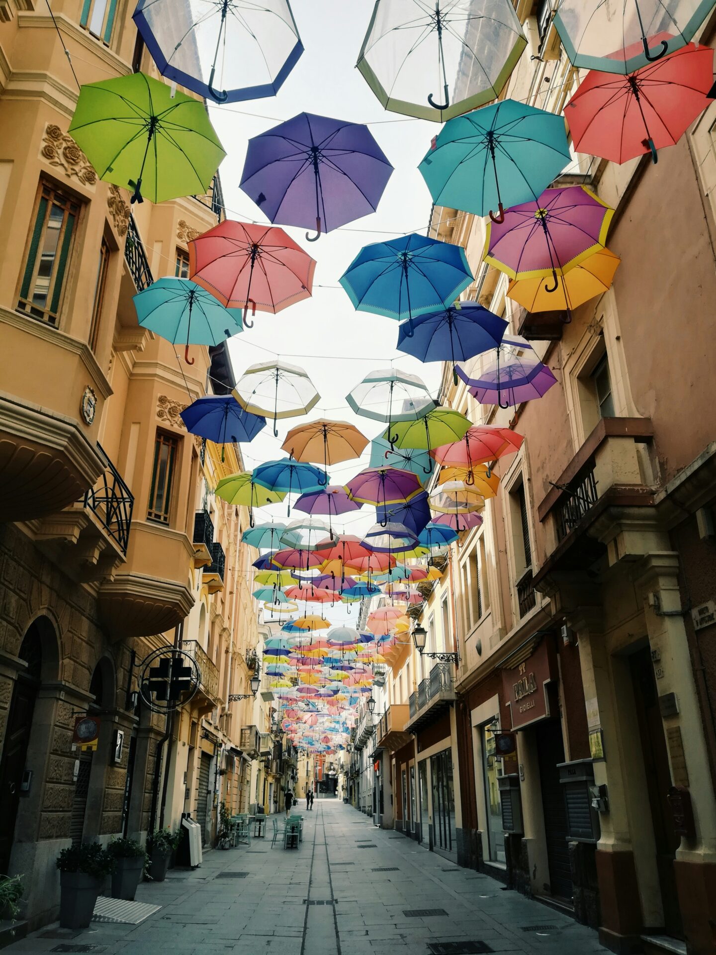 Charming street in Sardinia lined with colorful buildings, with vibrant floating umbrellas