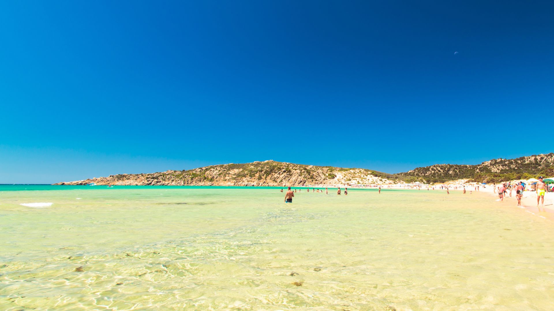 A sunny day at Su Giudeu beach in Sardinia, with clear turquoise water and people enjoying the shoreline.
