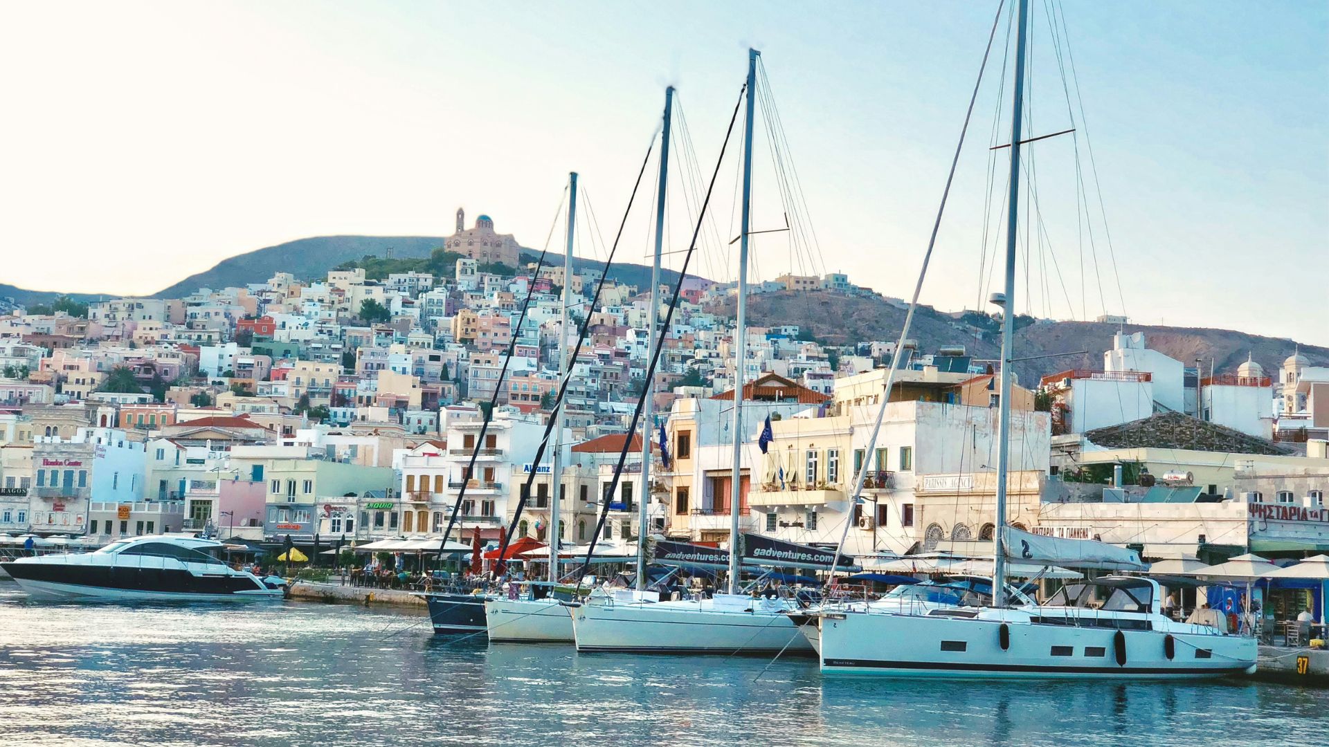 Colorful harbor scene in Syros, Cyclades, with boats and hillside buildings.