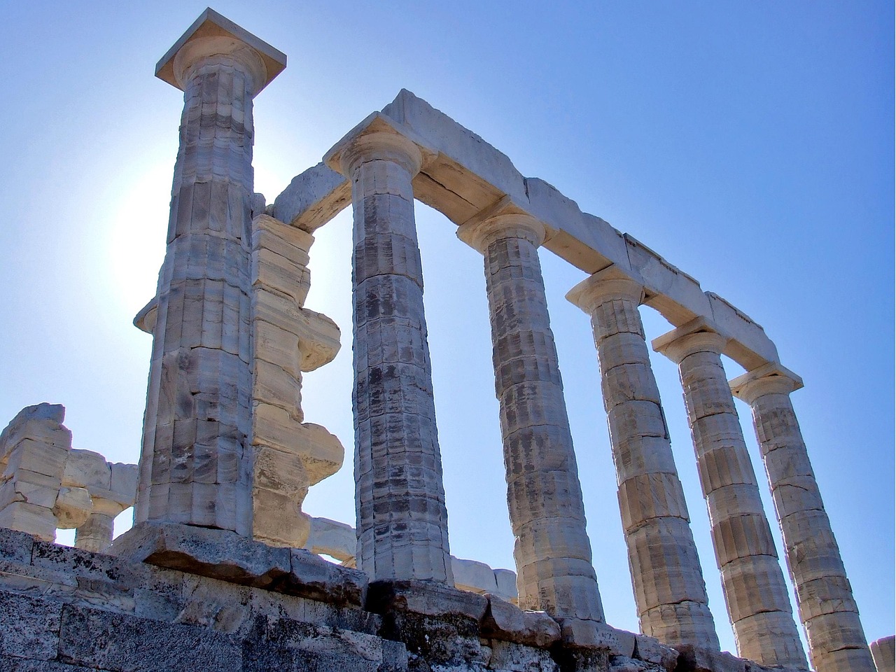 Close-up view of the ancient marble columns of the Temple of Poseidon at Cape Sounion, Greece, against a clear blue sky.