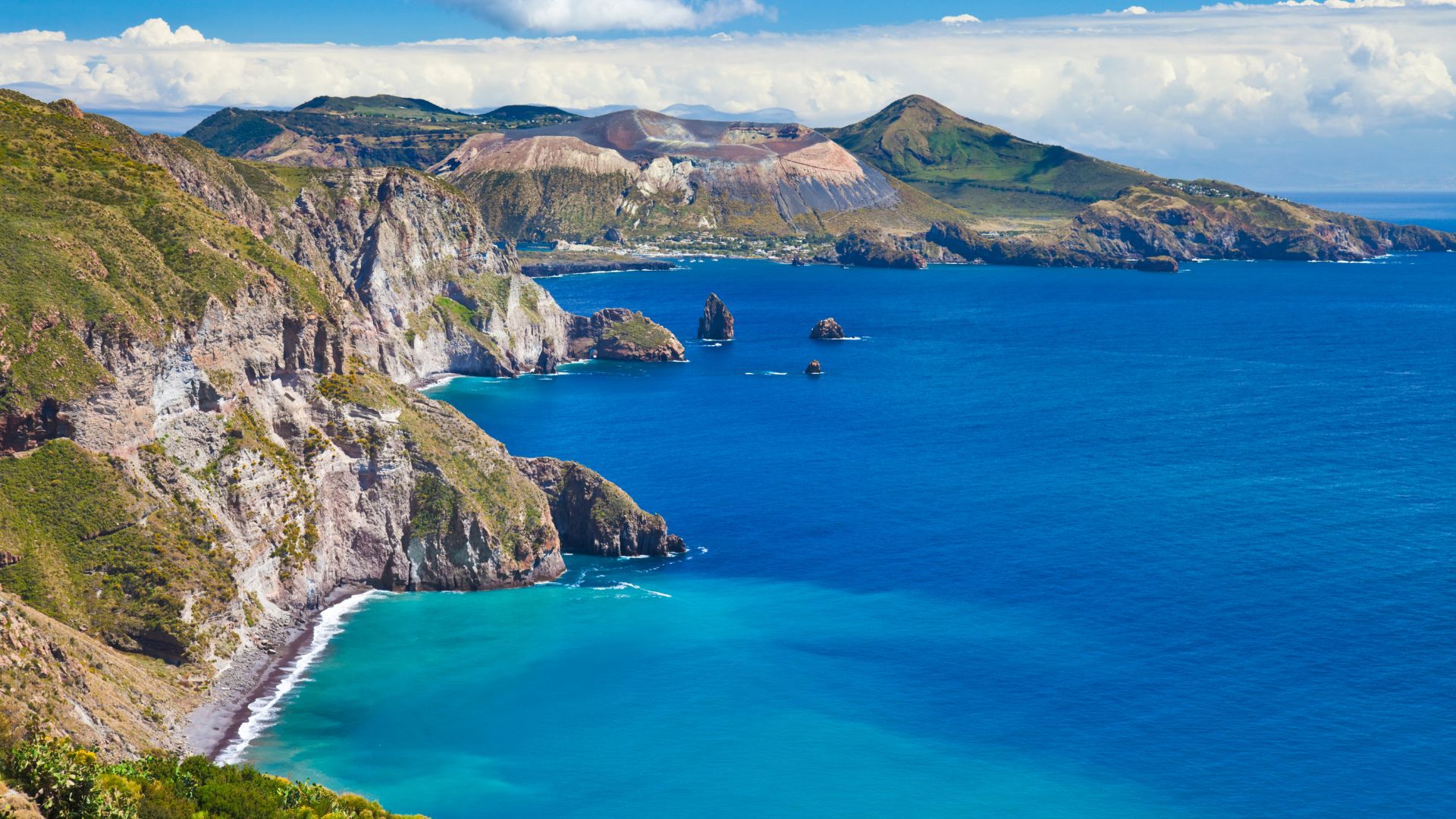 A scenic view of Vulcano Island, part of the Aeolian Islands in Italy, featuring its rugged volcanic terrain, rocky coastline, and the deep blue sea surrounding it.