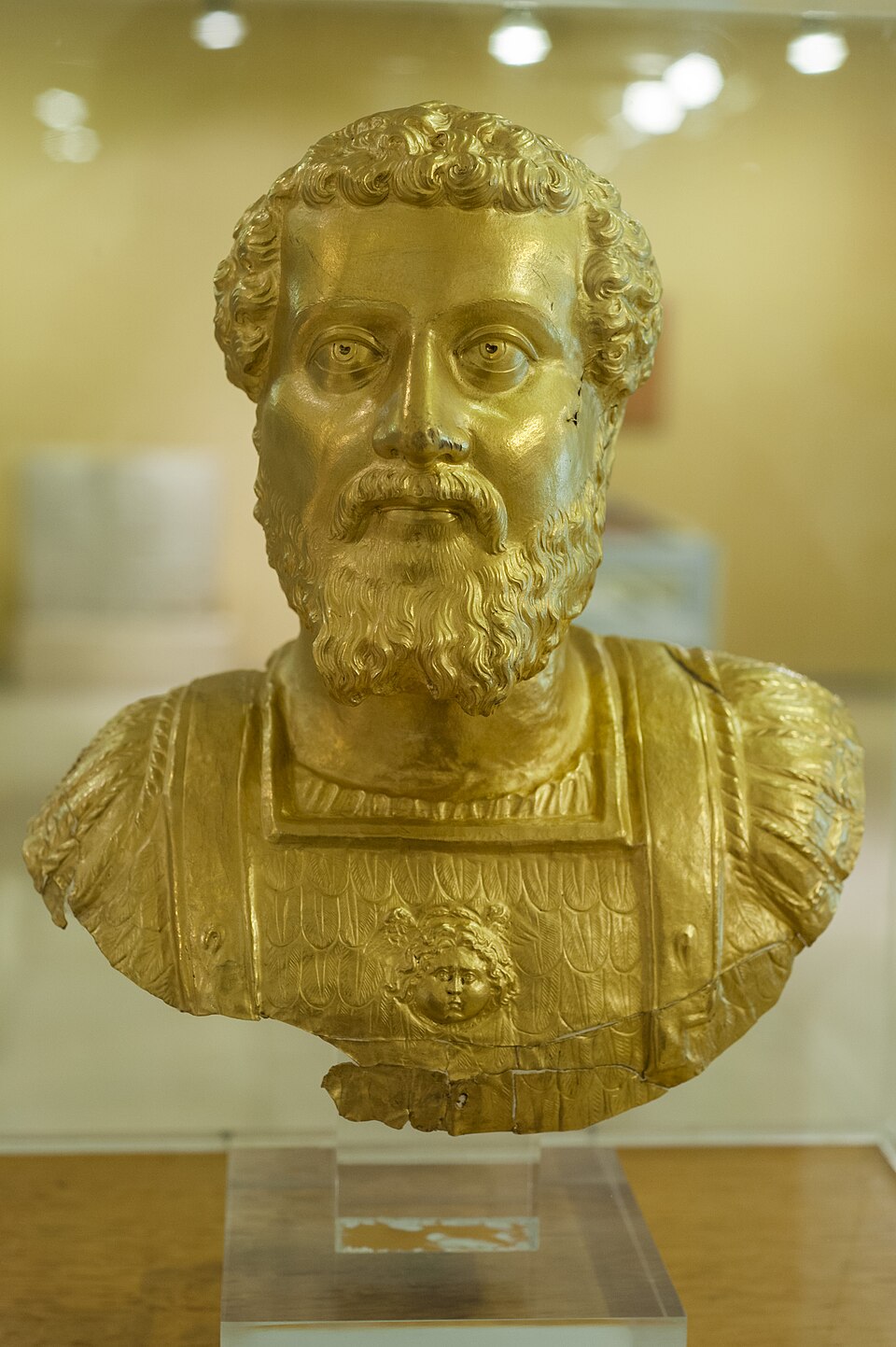 Golden bust of a male figure from ancient Plotinopolis, displayed on a pedestal.