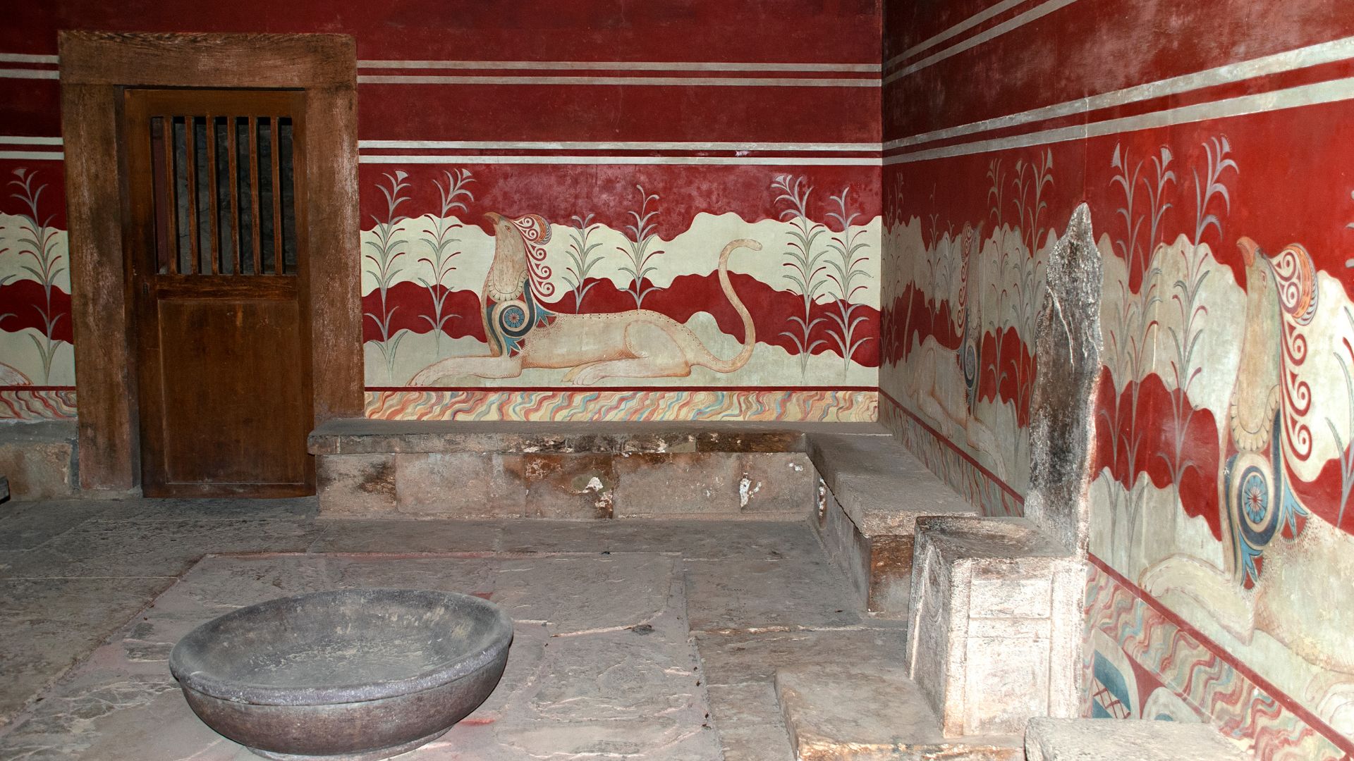 A chamber within the Minoan palace complex featuring a stone chair, and walls are adorned with frescoes, including representations of griffins,