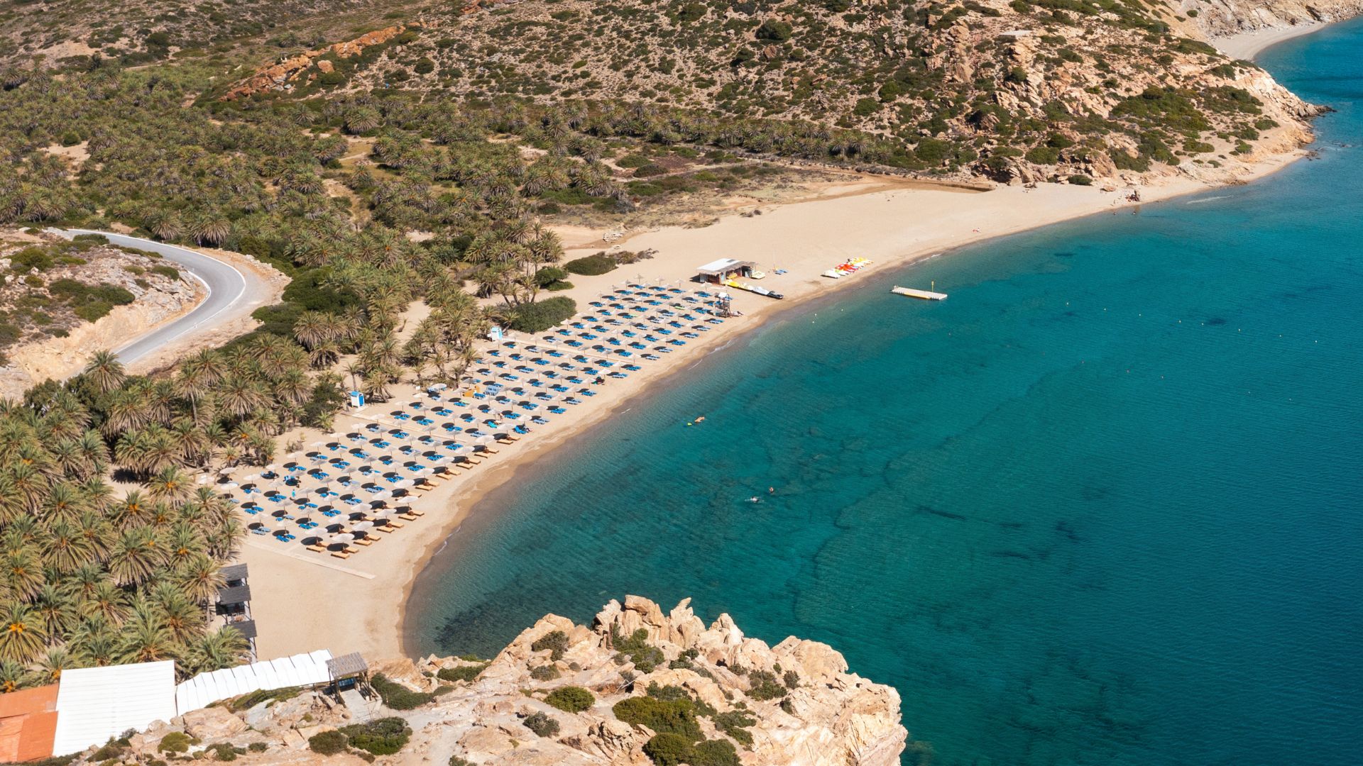 Aerial view of Vai Beach with palm trees and beach umbrellas.
