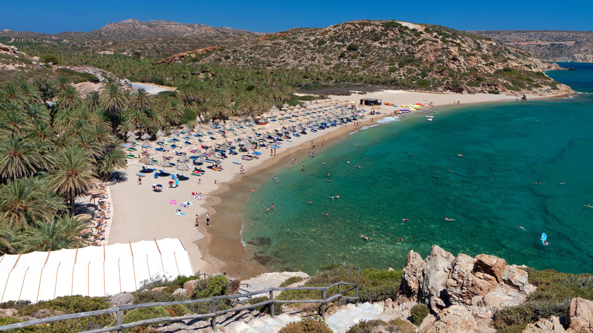 Scenic view of Vai Beach with palm trees and beach umbrellas.
