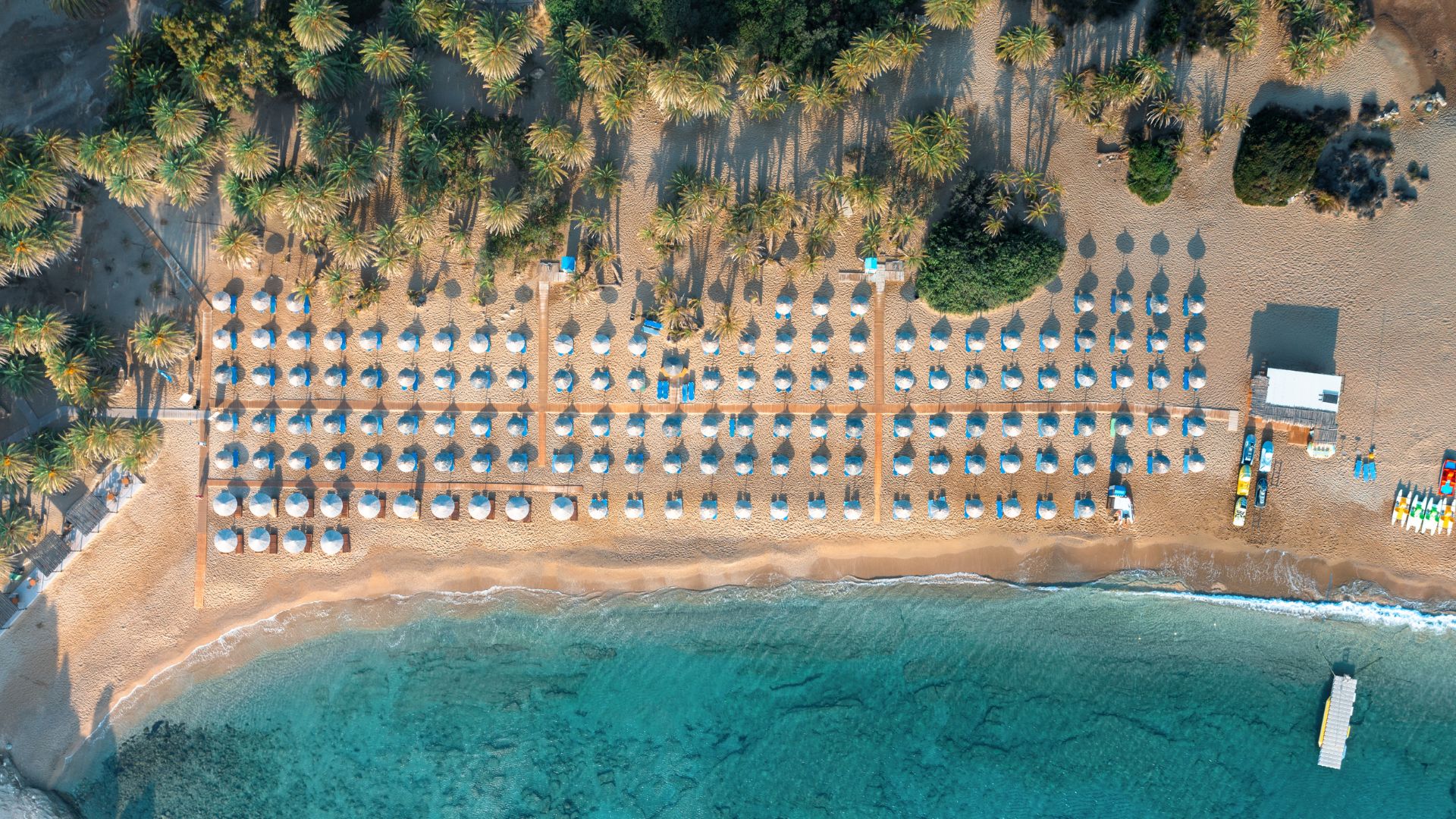 Aerial view of Vai Beach with palm trees and beach umbrellas.