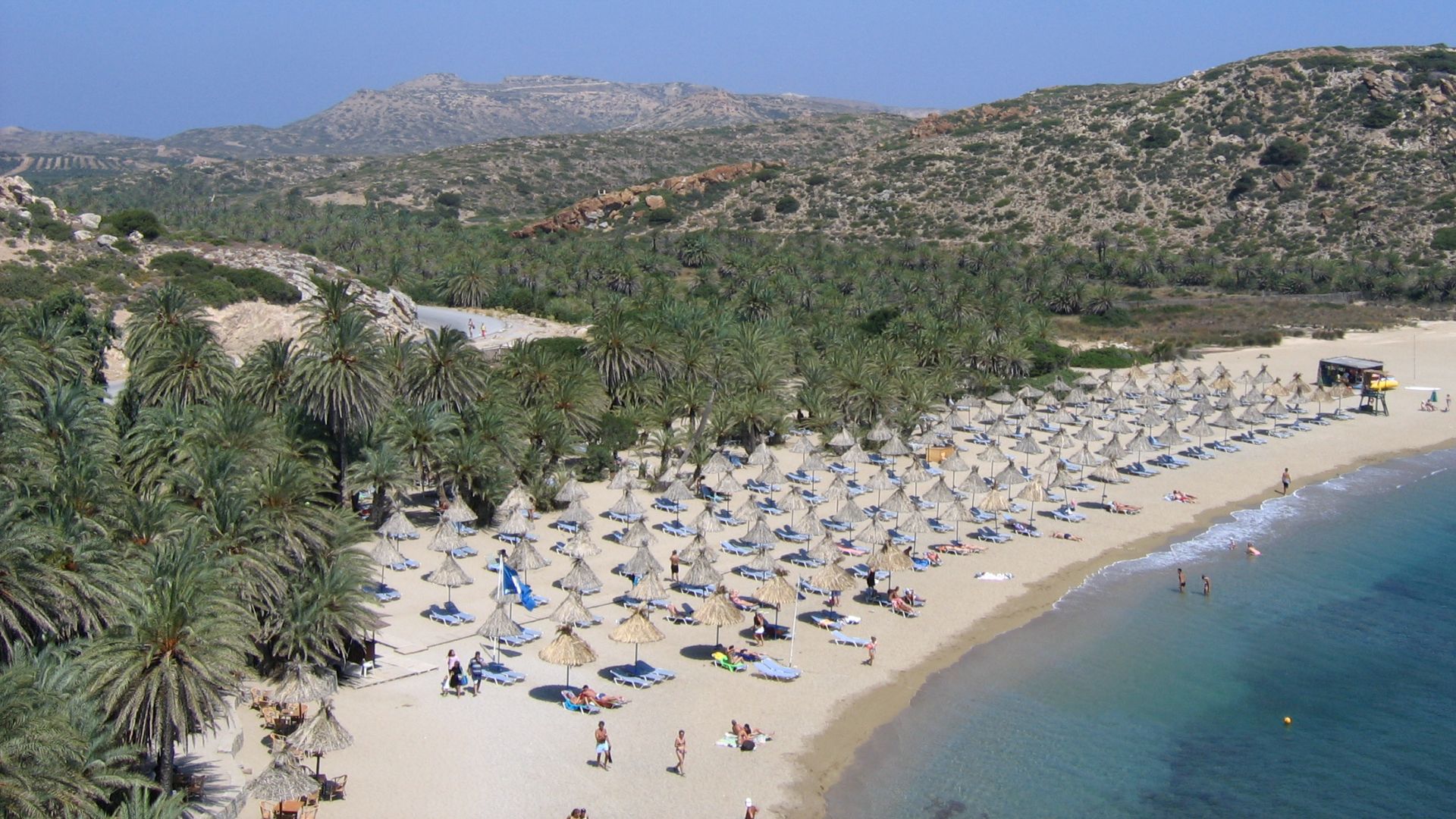 Aerial view of Vai Beach with palm trees and beach umbrellas.