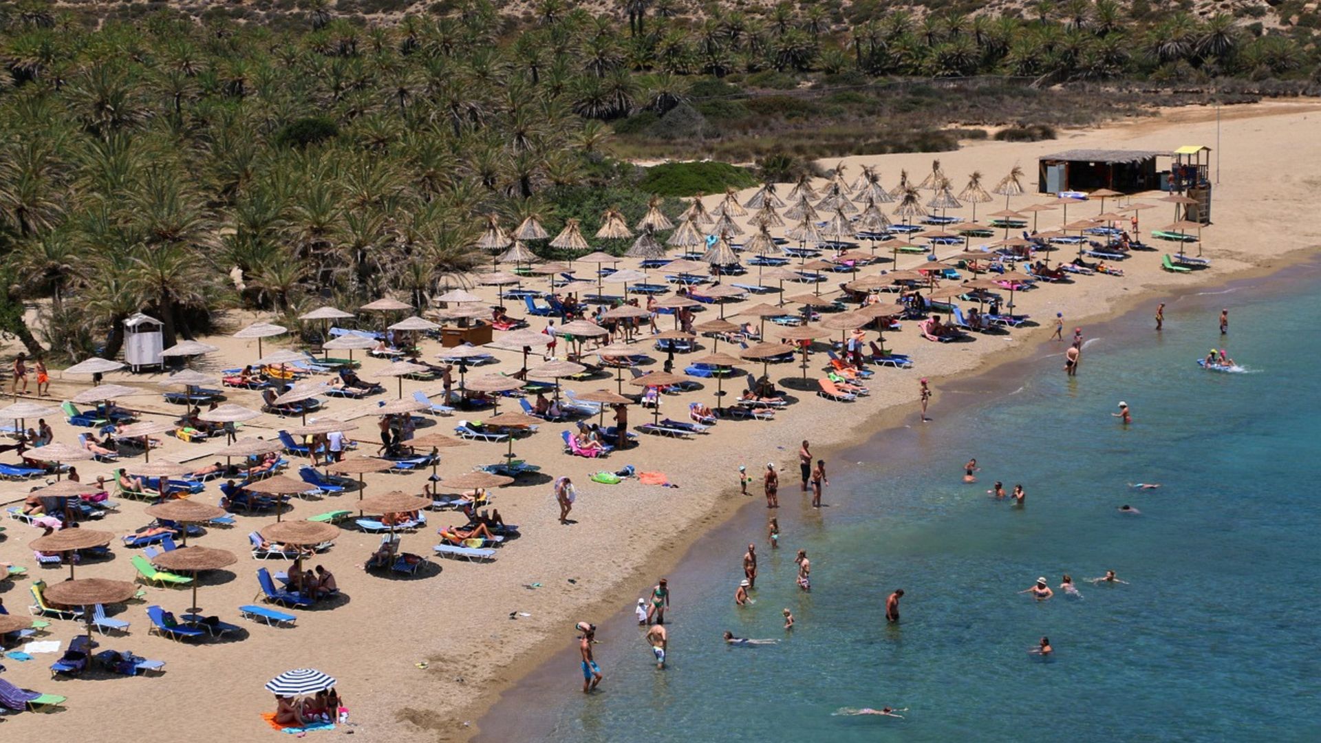 Scenic view of Vai Beach with palm trees and beach umbrellas.