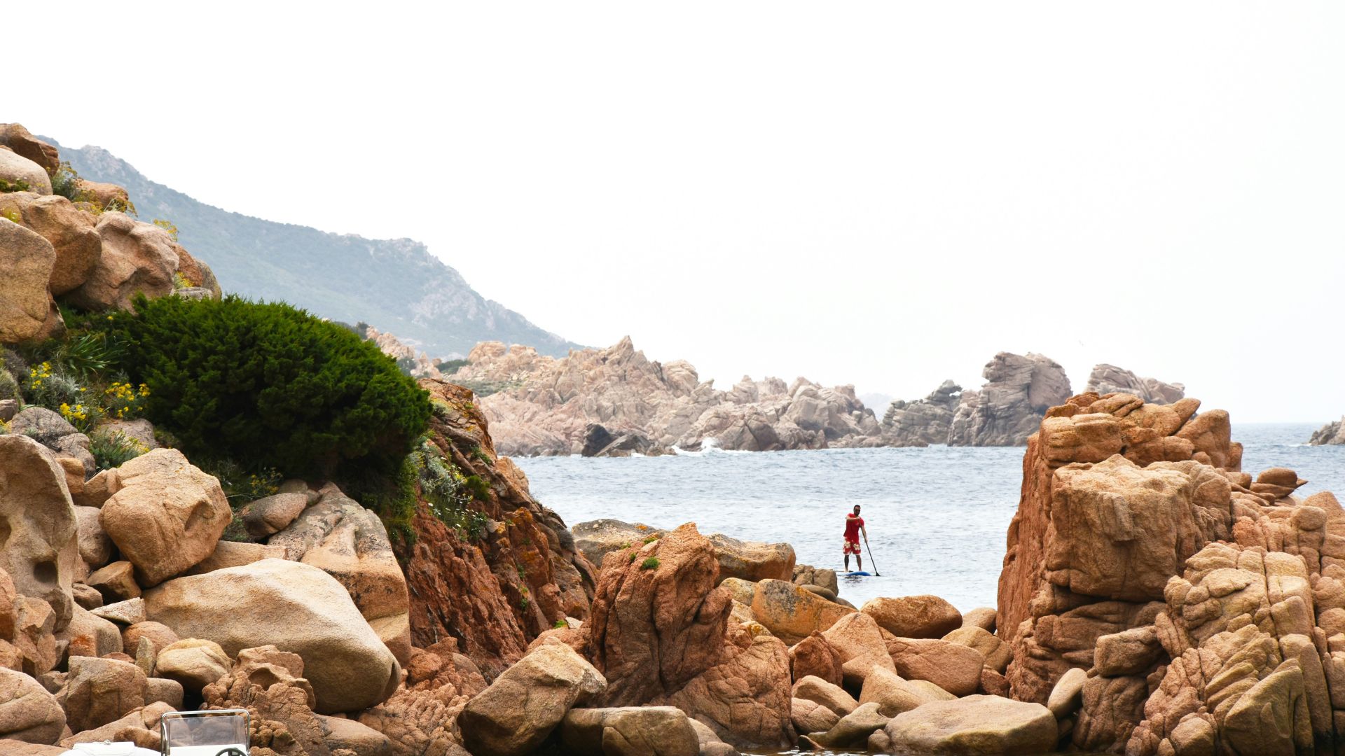Rocky coastline of Valle della Luna in Capo Testa with a person paddleboarding in the distance