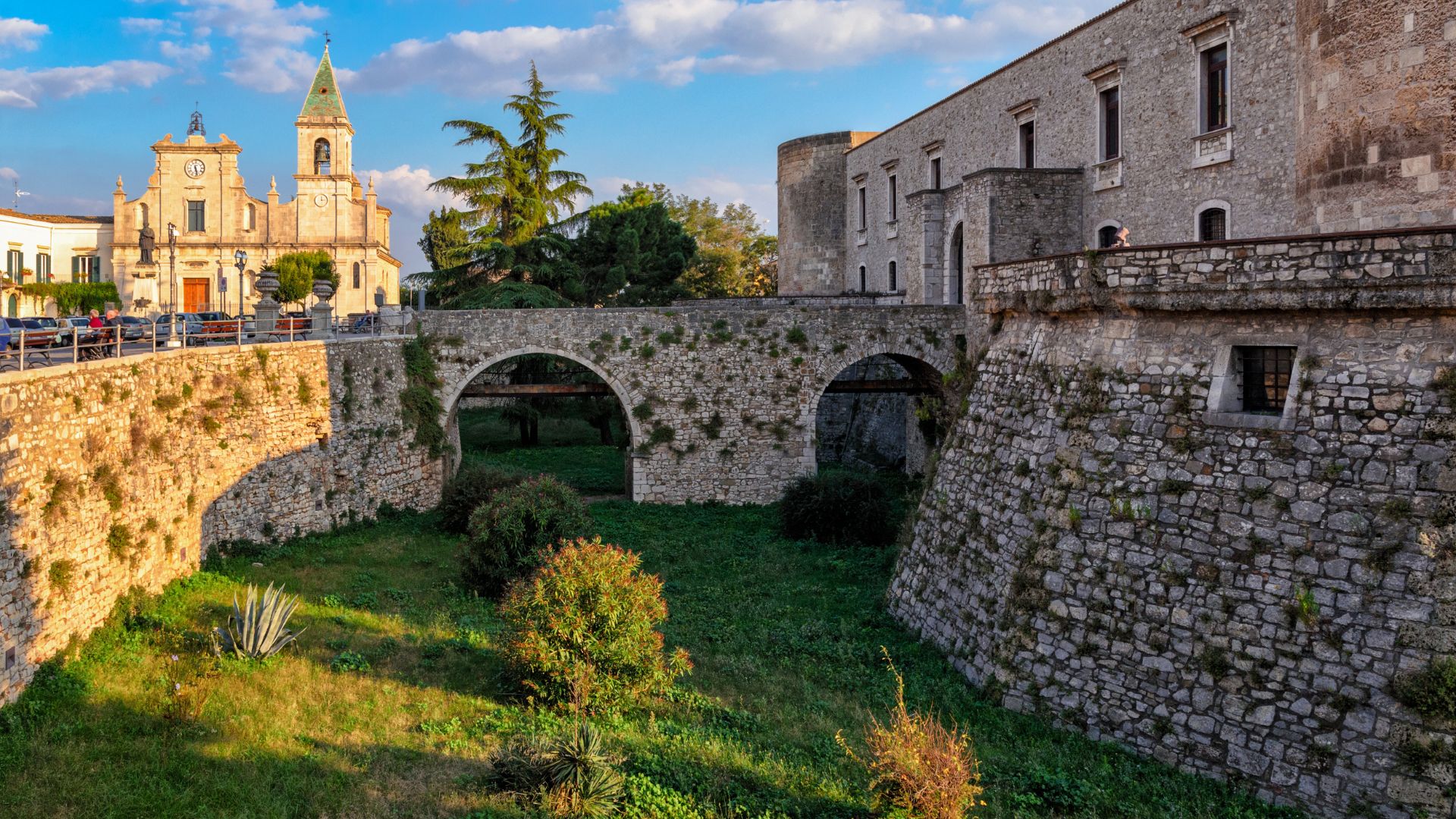 The image shows Aragonese Castle (Castello di Venosa) standing on on a plateau between two valleys, surrounded by vegetation located in Venosa, in the province of Potenza, Basilicata, Italy.