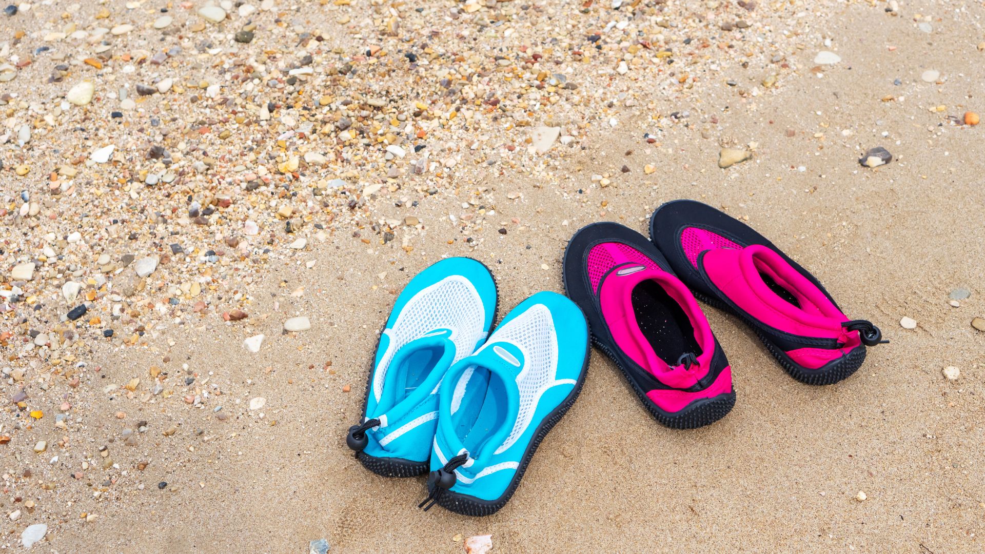 A blue and a pink watershoe on a white sand. 