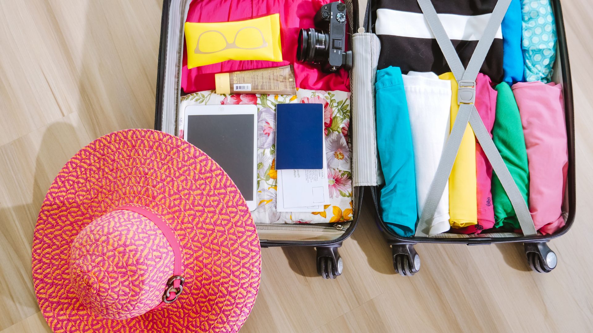 A travelling bag with a beach hat, clothes, sunscreen, sunglasses, camera and other beach essentials.