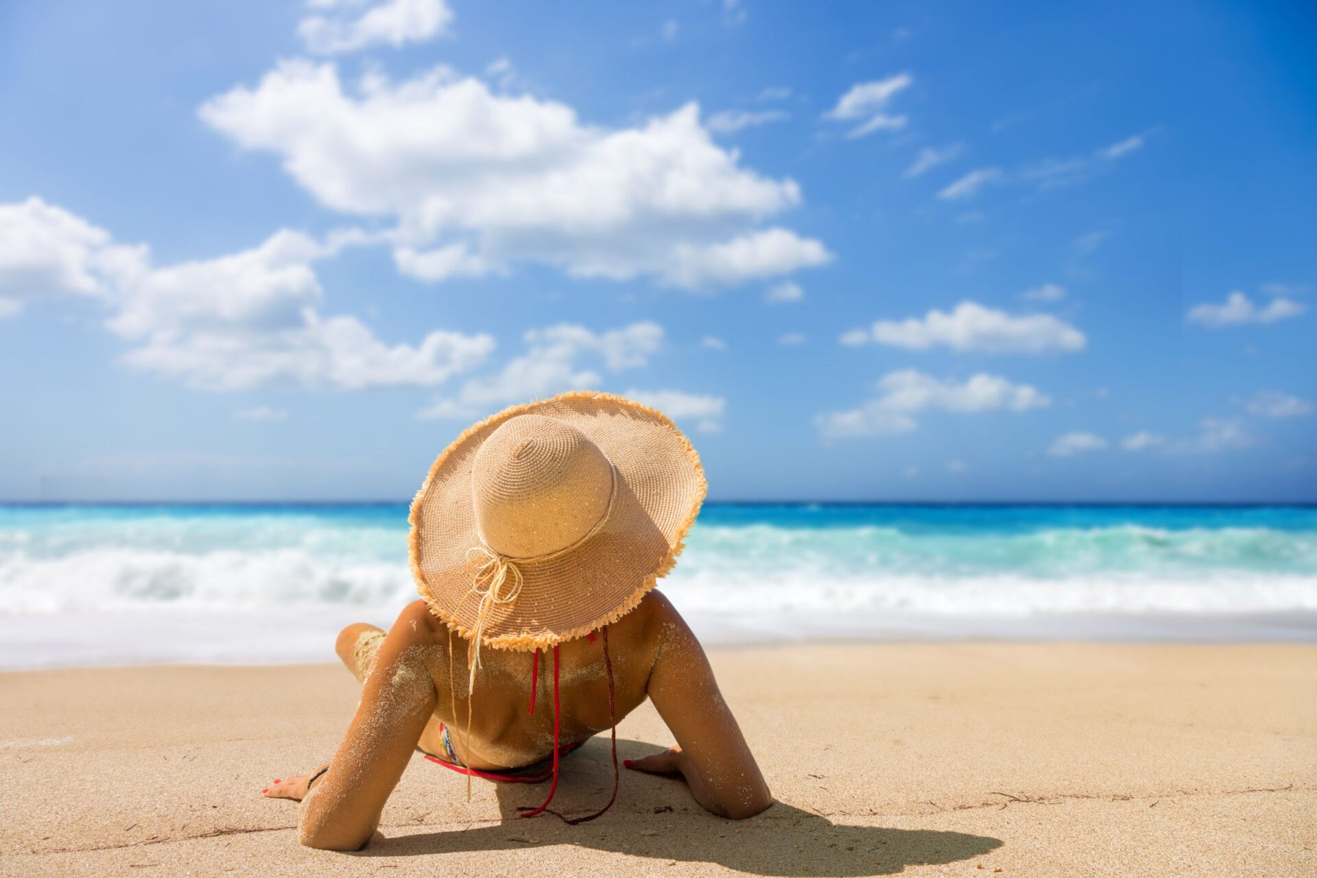 woman lying on the beach with a brimmed hat