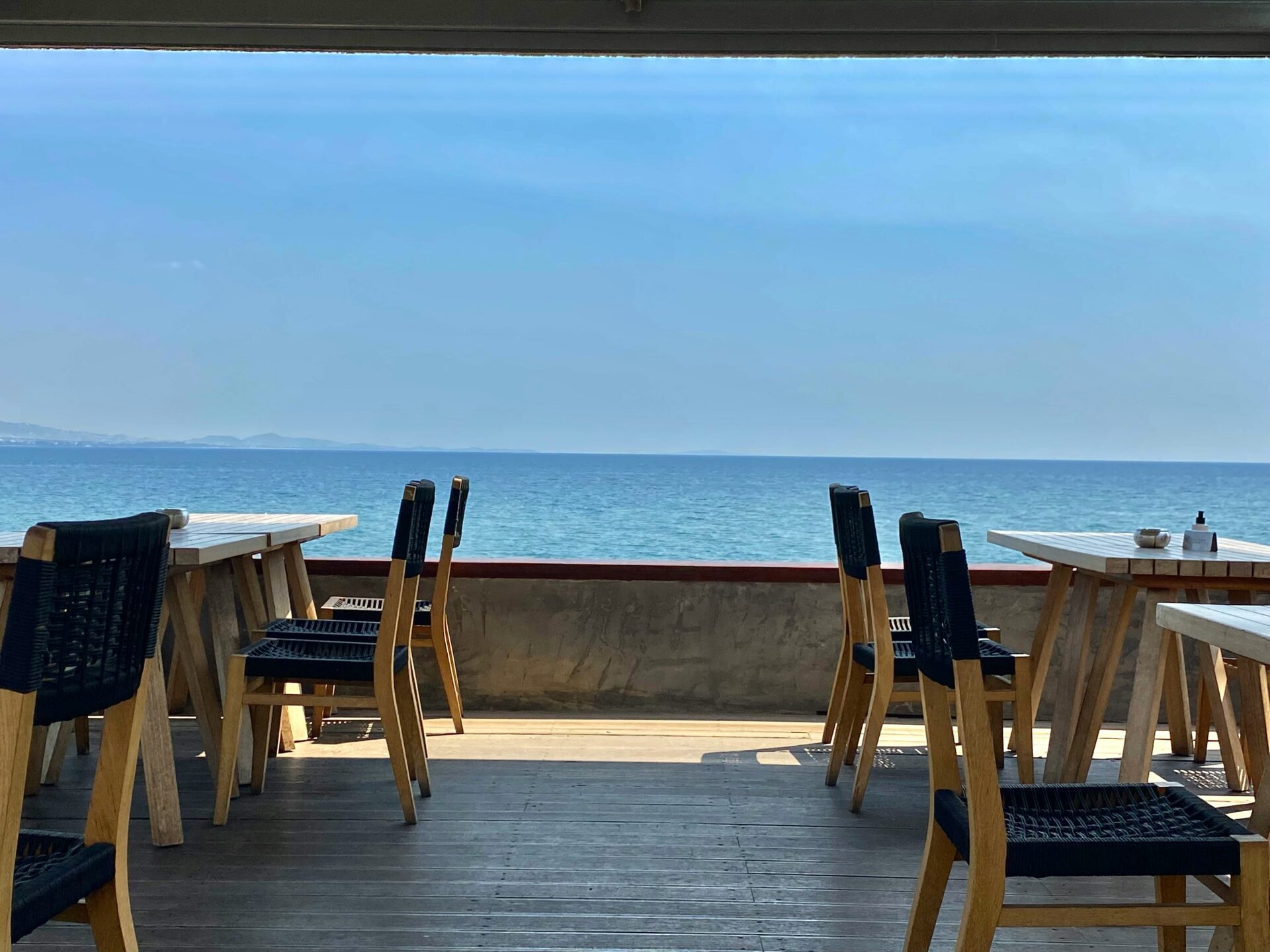 A beach side restaurant with tables and chairs over viewing the sea waters - Athens, Greece