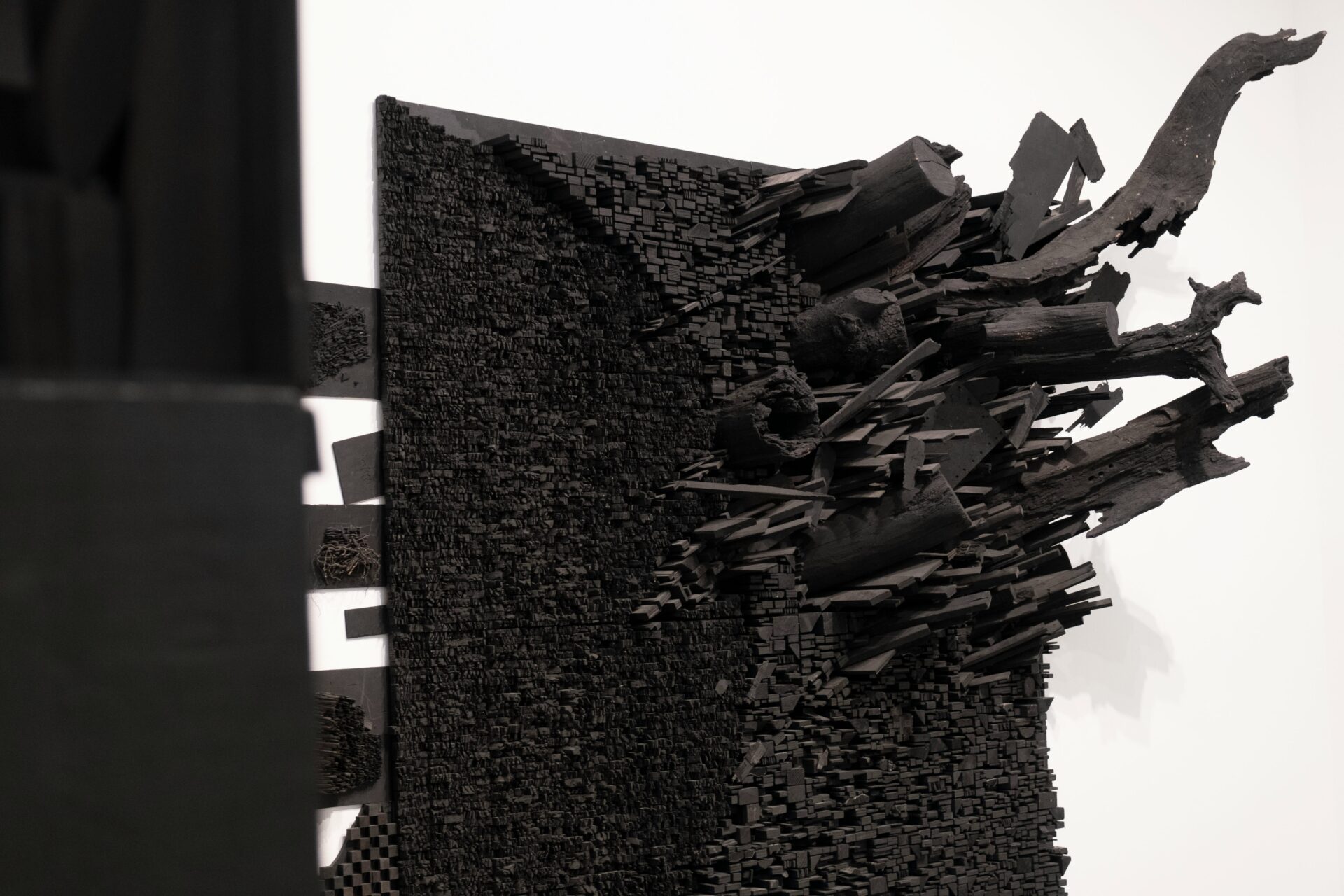 A black, abstract wall sculpture made of charred wood and geometric forms, displayed in a gallery at the Tate Museum