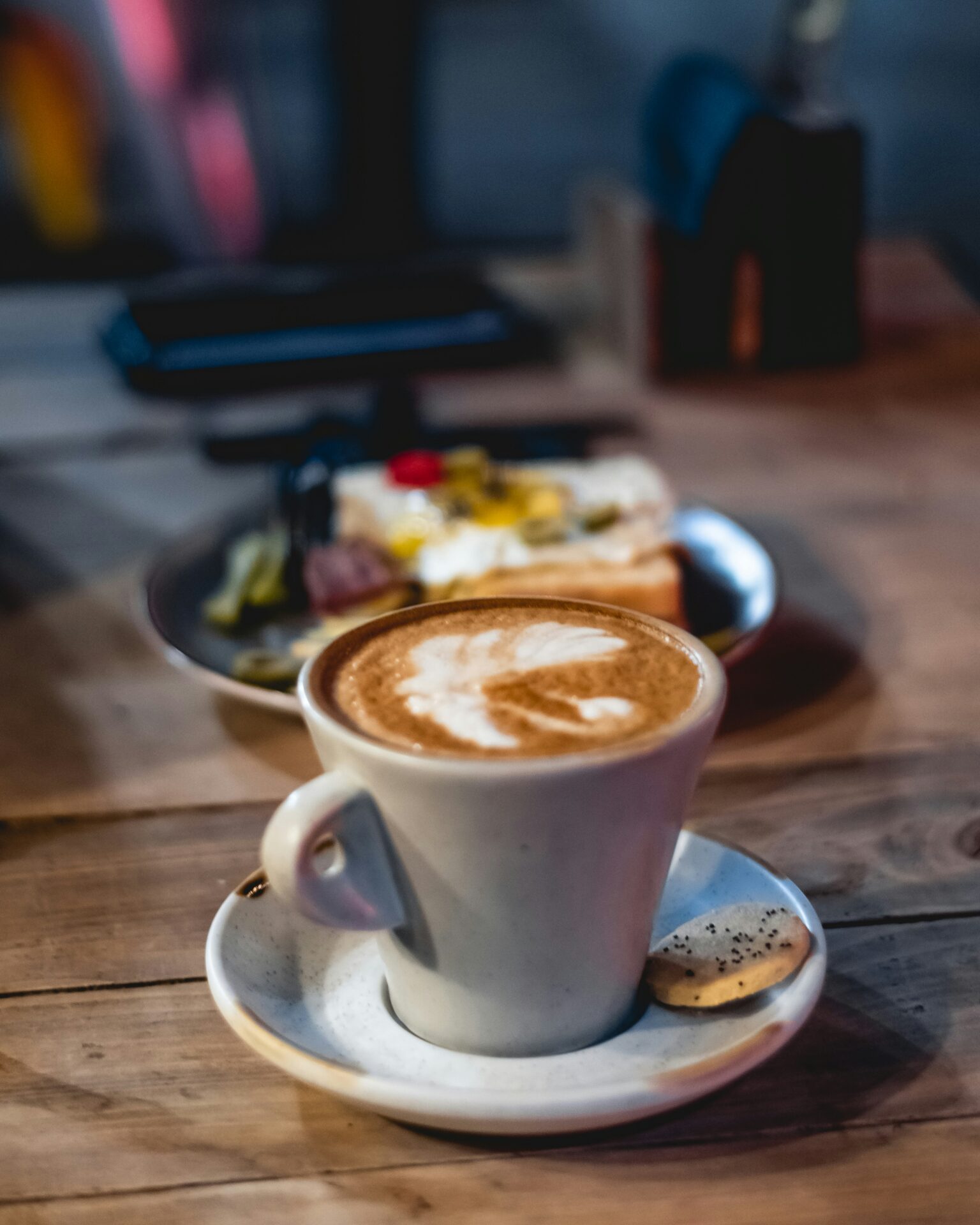 A cup of coffee latte served on a wooden table with a plate of cafe pastry