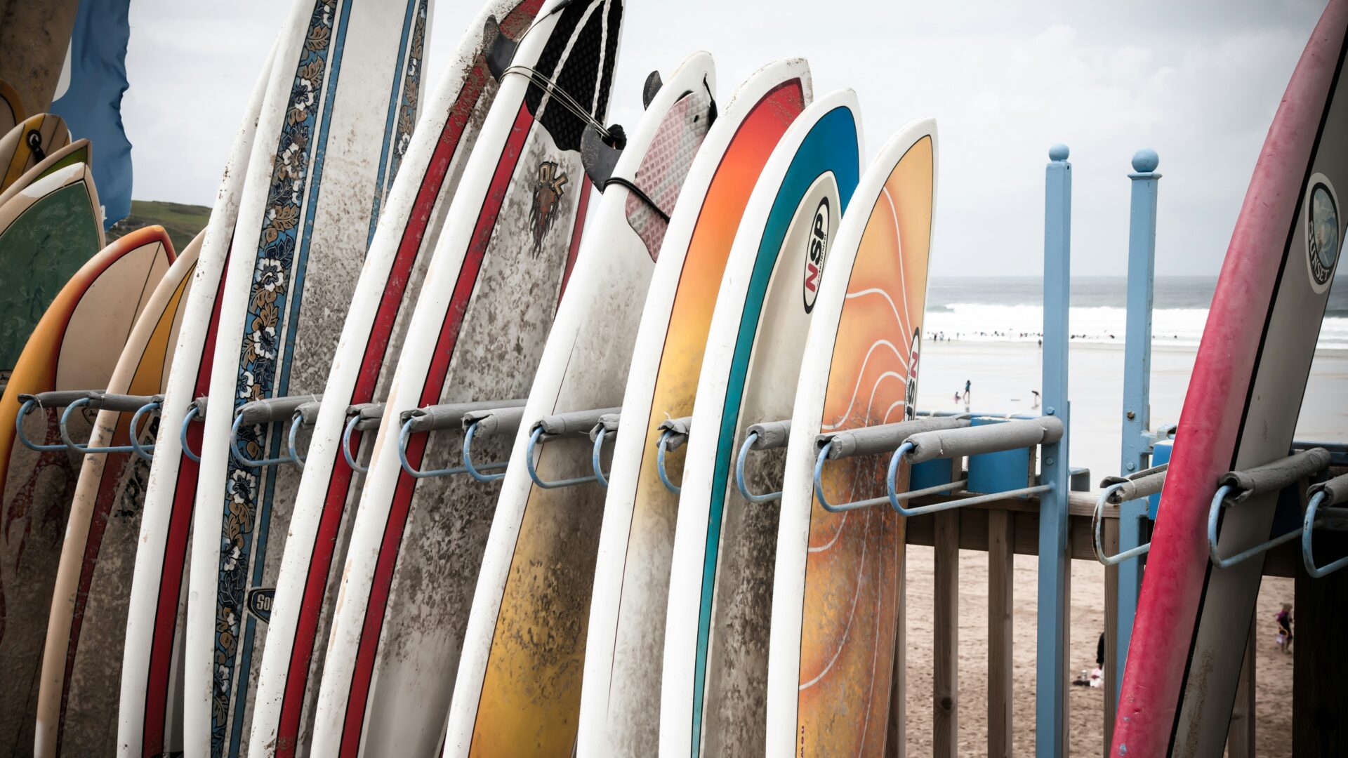 A surfboard resting against a brown wooden fence during daytime at Fistral Beach