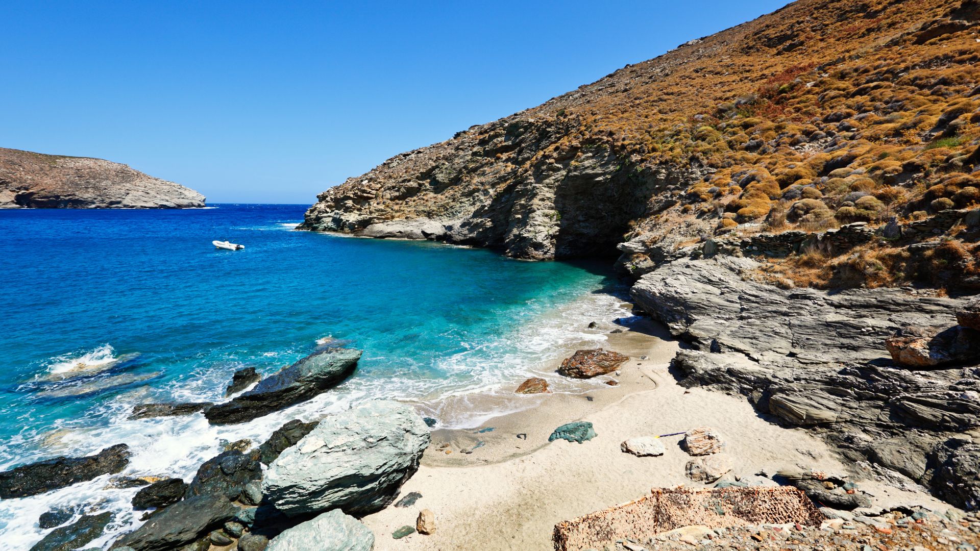  A scenic view of Achla Beach in Andros, Greece, with blue waters and rocky cliffs.
