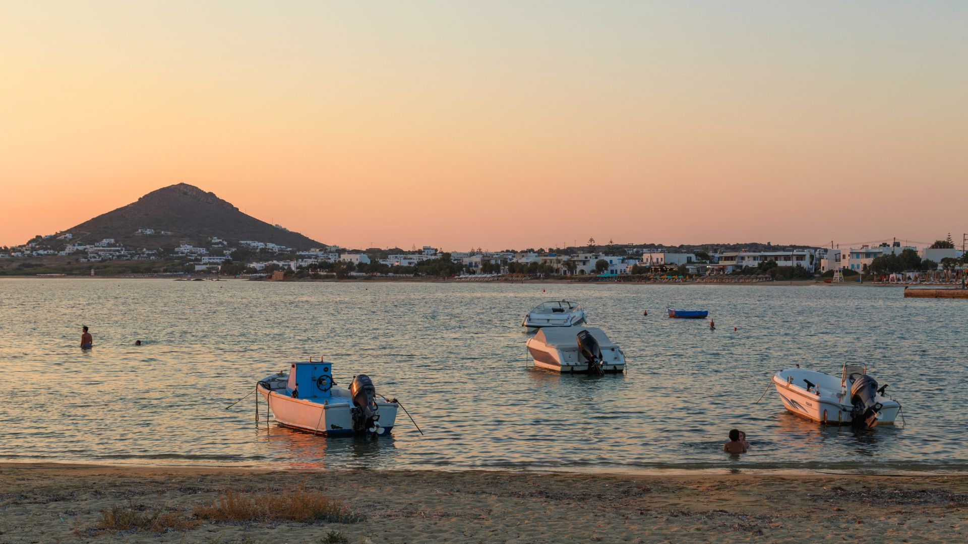 A scenic view of Agia Anna beach at sunset, with boats in the water and a hill in the background.