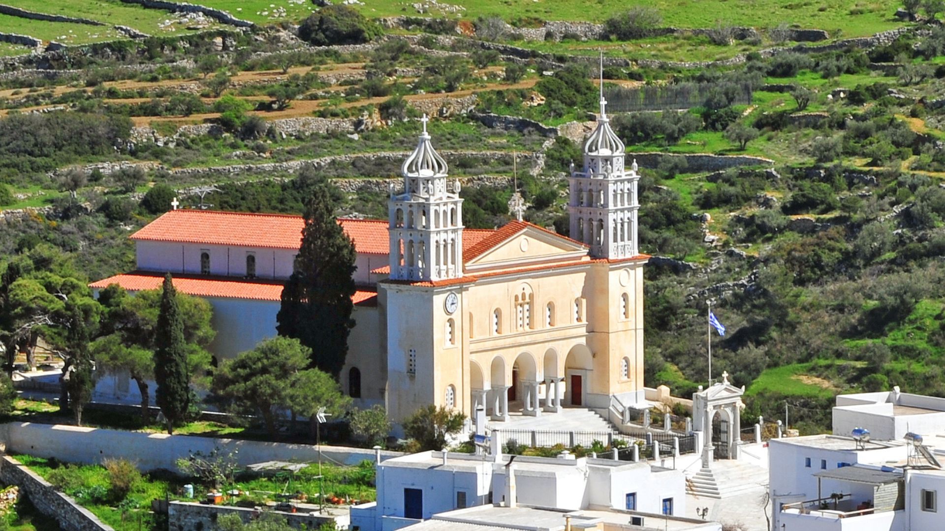 A whitewashed church with two bell towers stands prominently in a hillside village in Paros, Greece.