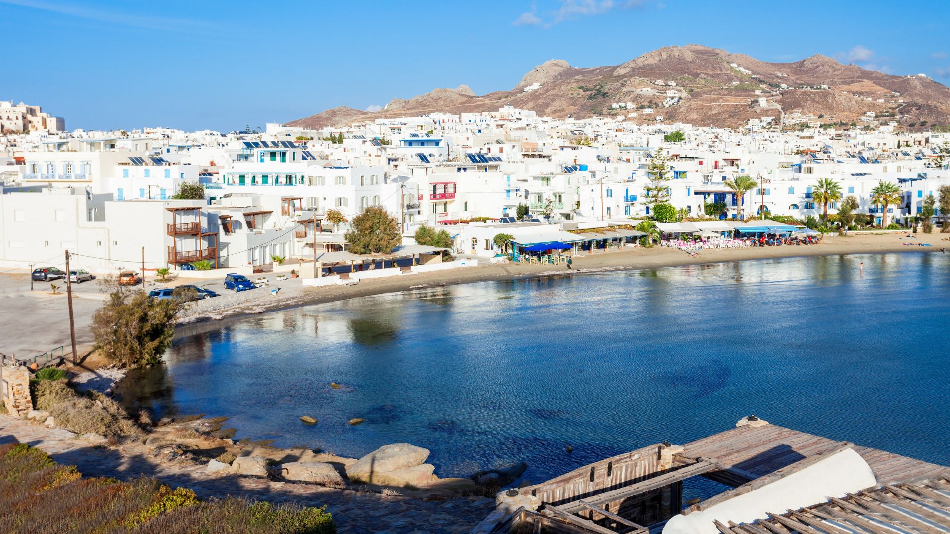 Scenic view of white building, mountains, and blue sea at Agios Georgios Beach in Naxos, Greece.
