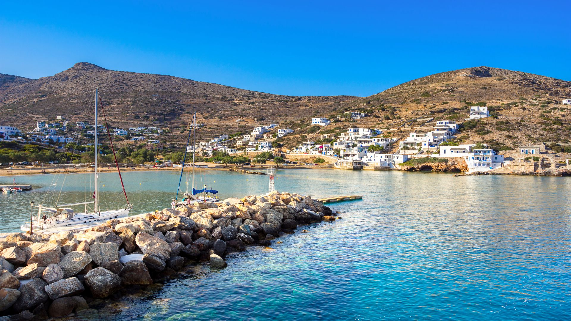 Sikinos, Greece: Scenic view of Alopronia port village with boats and whitewashed houses on a hillside.