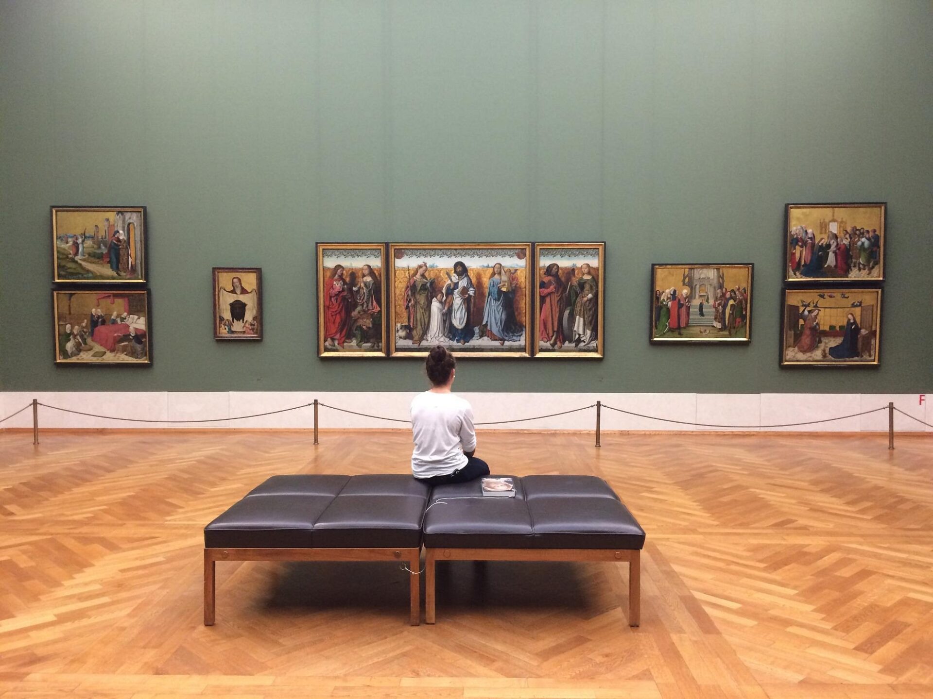 Interior of the Alte Pinakothek with large classical paintings mounted in ornate gold frames along neutral-colored walls.