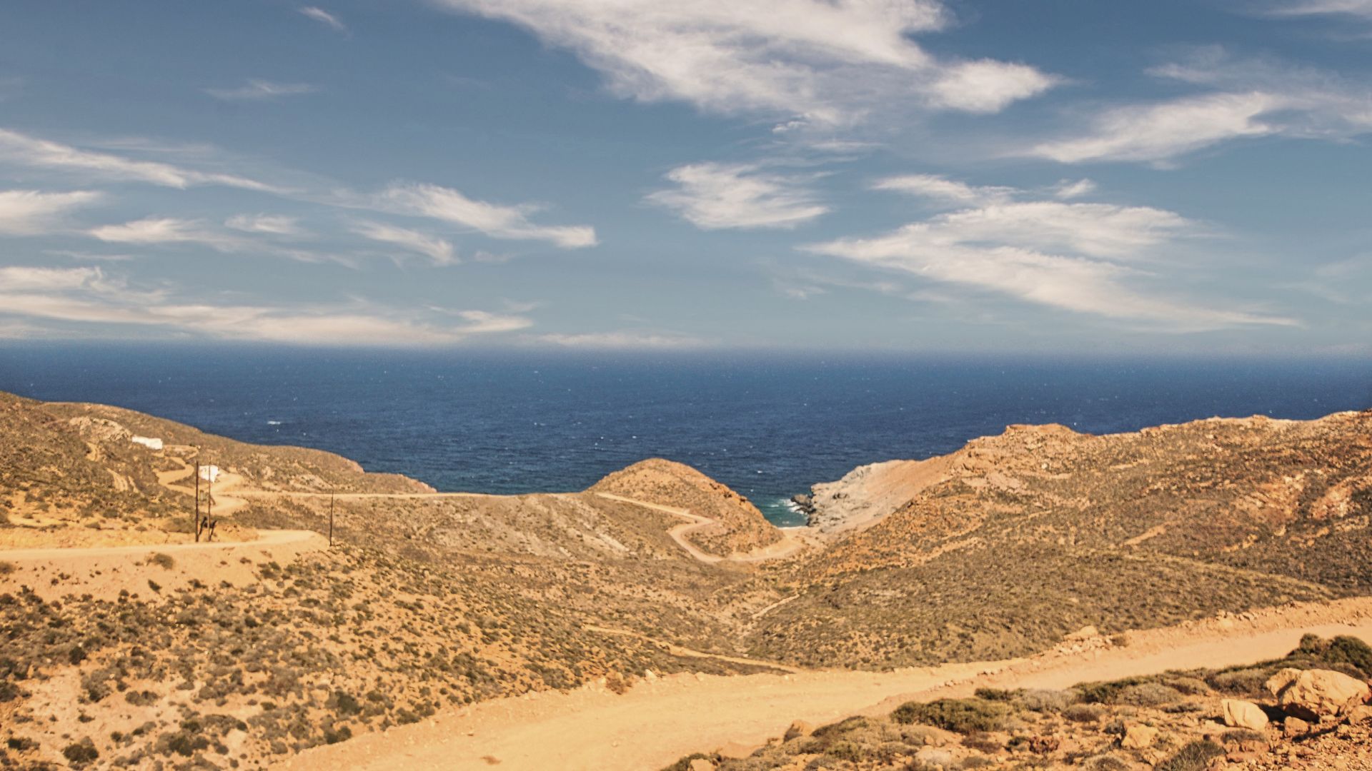 Arid Greek island landscape with hills, dirt roads, and the Aegean Sea under a blue sky, likely on Anafi near Kalamos.