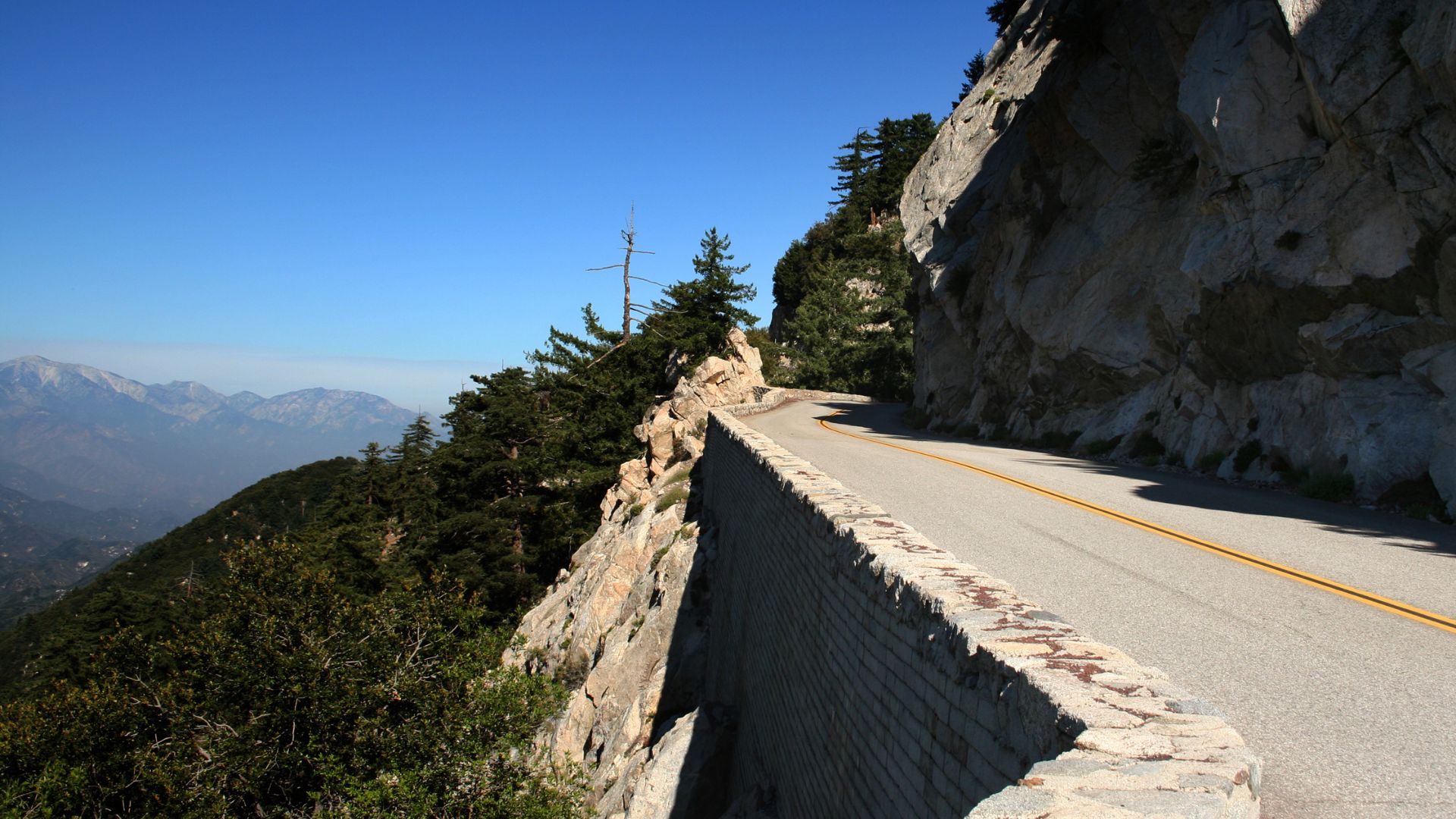 Angeles Crest Highway, Southern California: A winding mountain road with a stone retaining wall, showcasing the scenic beauty of the San Gabriel Mountains.