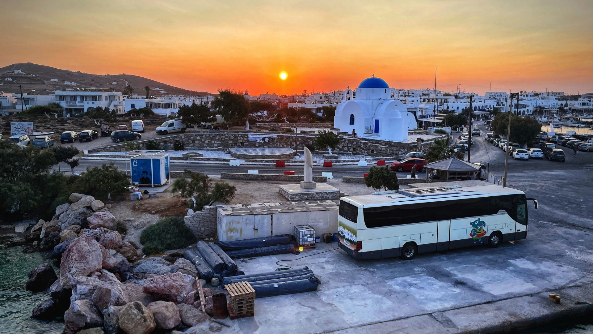 Sunset view in Antiparos, Greece, featuring a blue-domed church and a bus near the port.