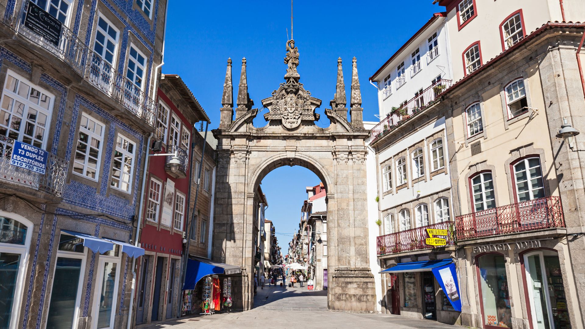 A stone archway, Arco da Porta Nova, stands between historic buildings on a sunny day in Braga, Portugal.