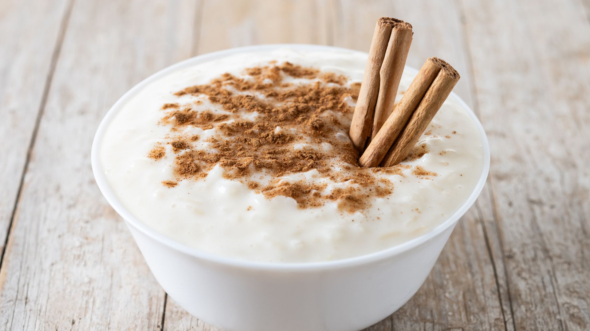 A creamy white pudding topped with ground cinnamon and cinnamon sticks.